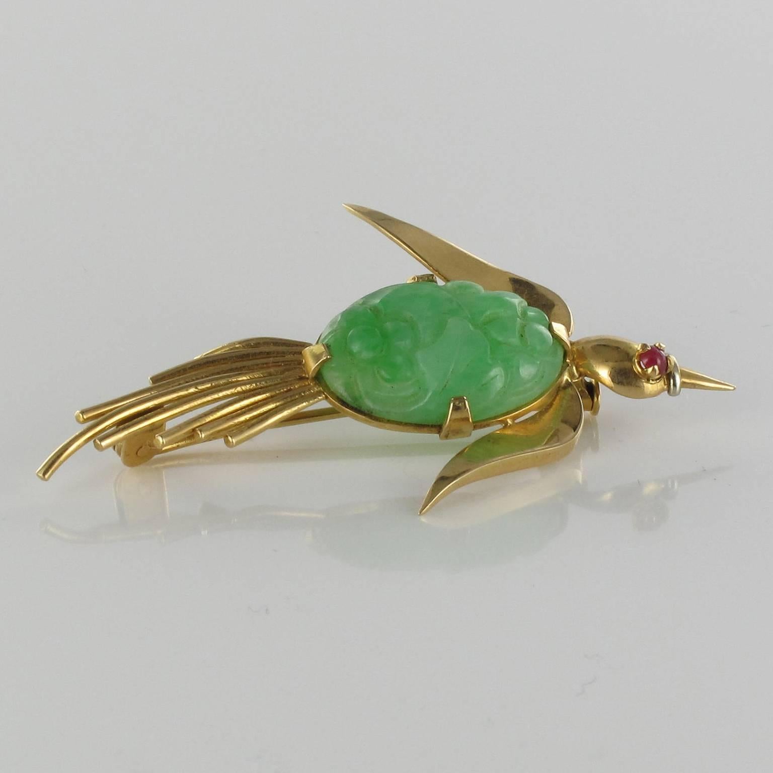 Brooch in 18 carats yellow gold.

This enchanting brooch features a bird in full flight with a flower engraved jade cabochon on its breast. Its eye is a red gem. 
The clasp of this jade brooch is a pin with a safety pump. 

Jade: Length: 2 cm,