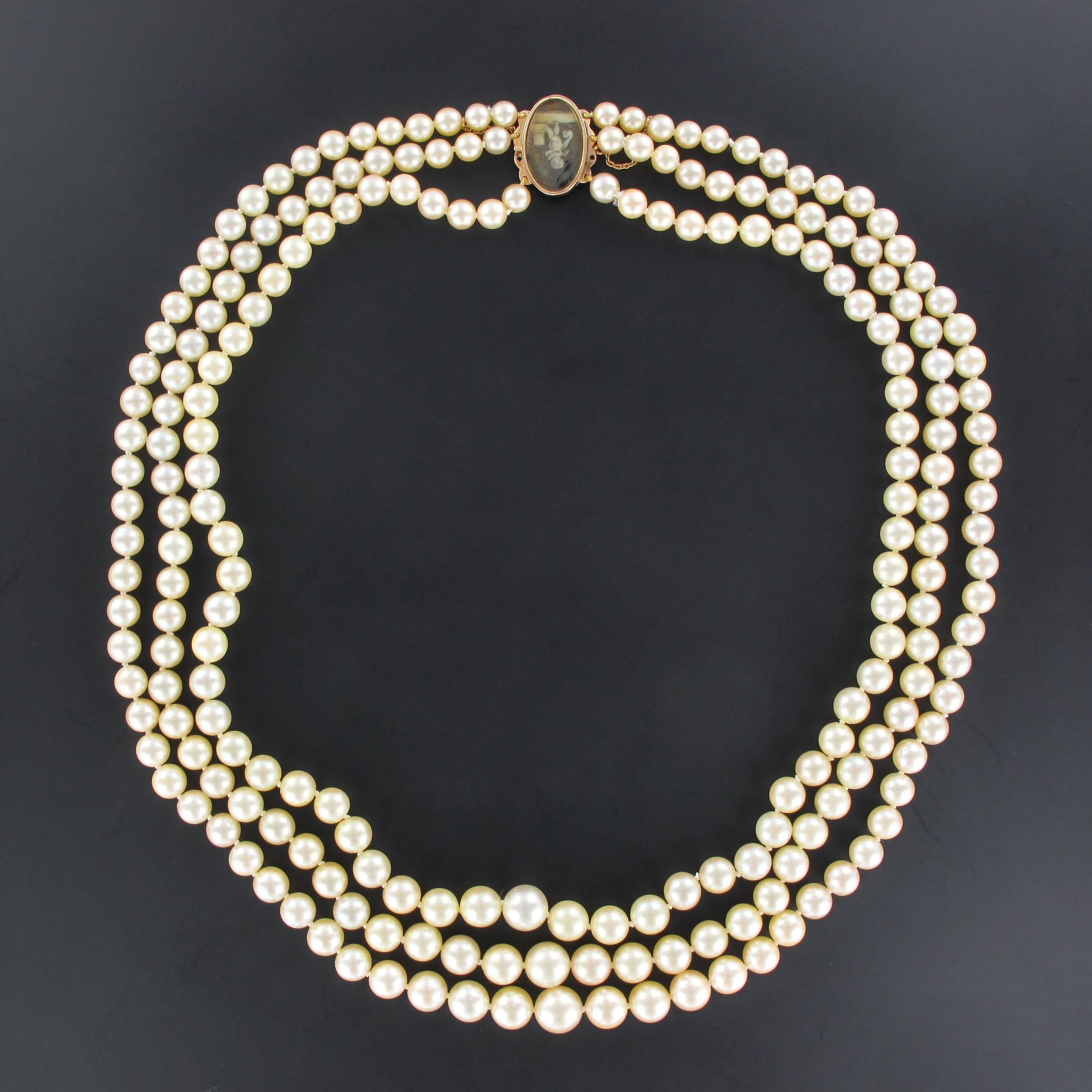 This  pearl necklace is composed of three strands of Japanese cultured pearls which are held together by an oval 18K rose gold clasp, french mixed hallmark. It is set with a miniature on enamel representing an anglelot and is accompanied by a safety