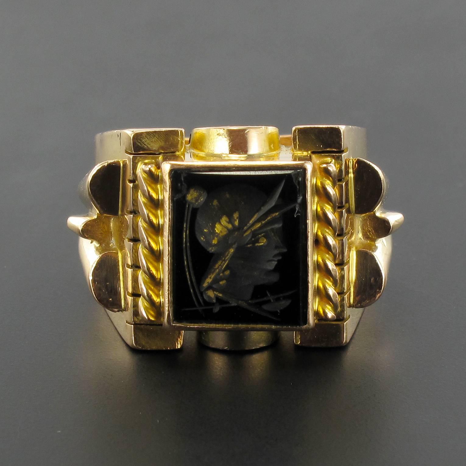 18 carat yellow gold ring, eagle head hallmark. 

This superb signet ring is bezel set with a square intaglio in onyx representing a helmeted warrior partially decorated with gold leaf. On each side are gold braids, the solid mount is set at each