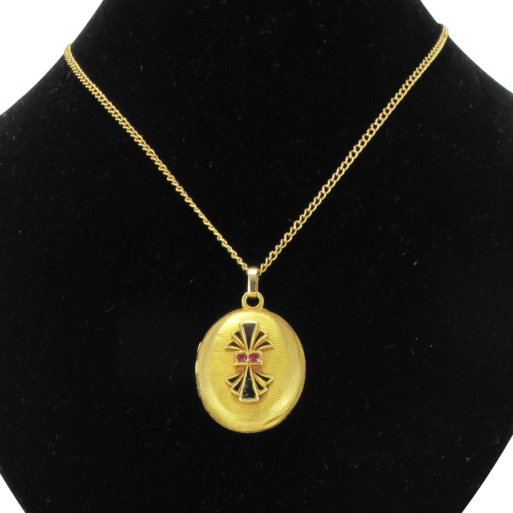 18 karat yellow gold medallion.
This antique engraved gold locket is set with a double fan design in black enamel set with 2 round rubies. The medallion locket opens with a side hinge to reveal a crystal screen edged with gold to protect a small