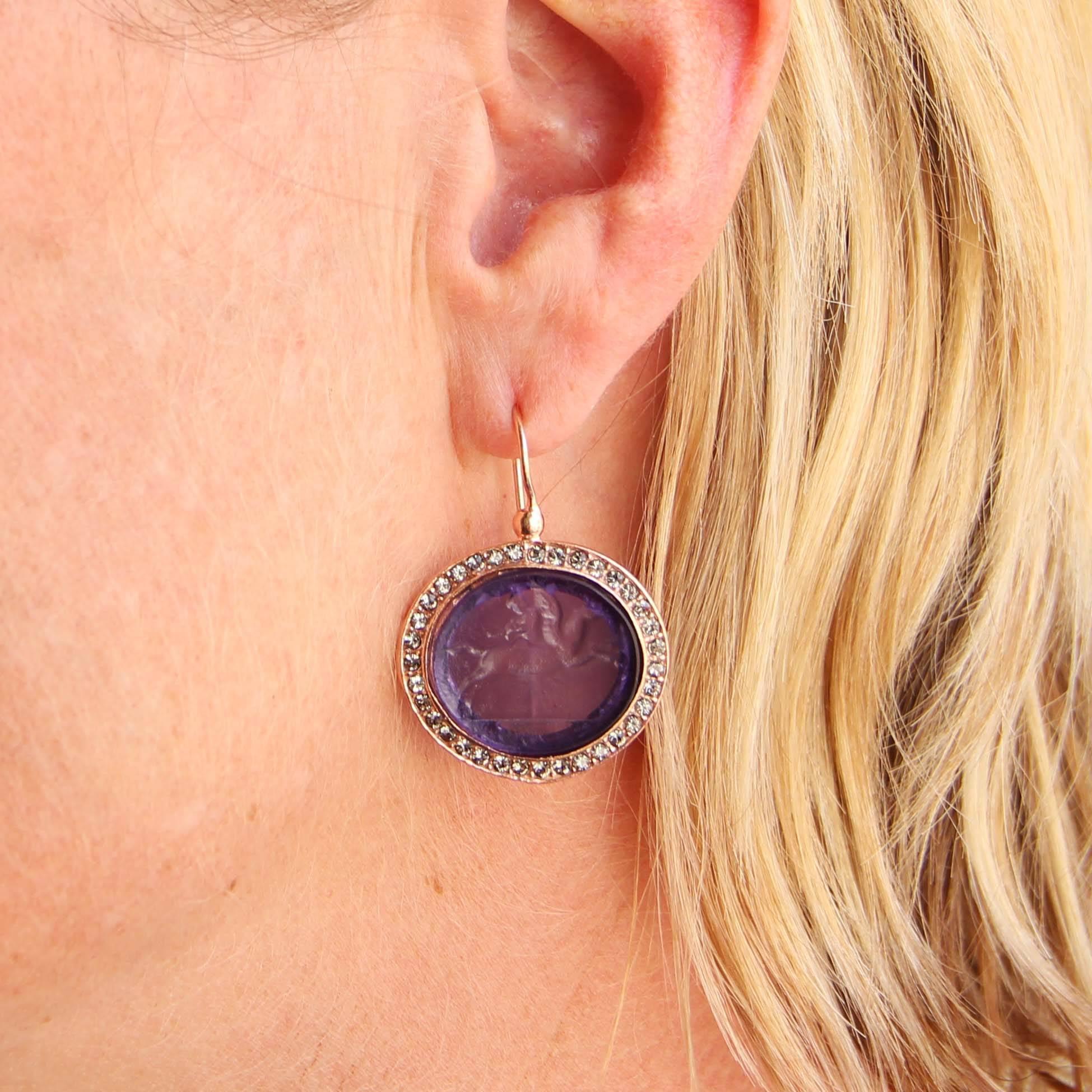 For pierced ears.

Pair of earrings in vermeil, silver and rose gold.

Drop earrings are set by a violet cameo on glass paste surrounded by crystals. The clasps are goosenecks with safety hooks. 

Height: 3,6 cm, width at the cameo: 2,5 cm.
Total
