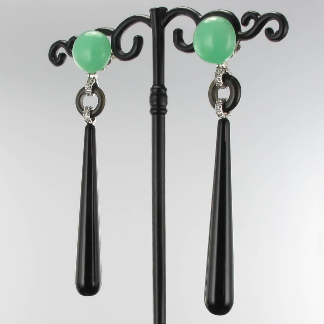 For pierced earrings.

Earrings in 18 carat white gold.

Each dangle earring is composed of a chrysoprase cabochon which holds a curved disc of onyx set with a line of brilliant-cut diamonds itself retaining a drop of onyx. The clasp is a large