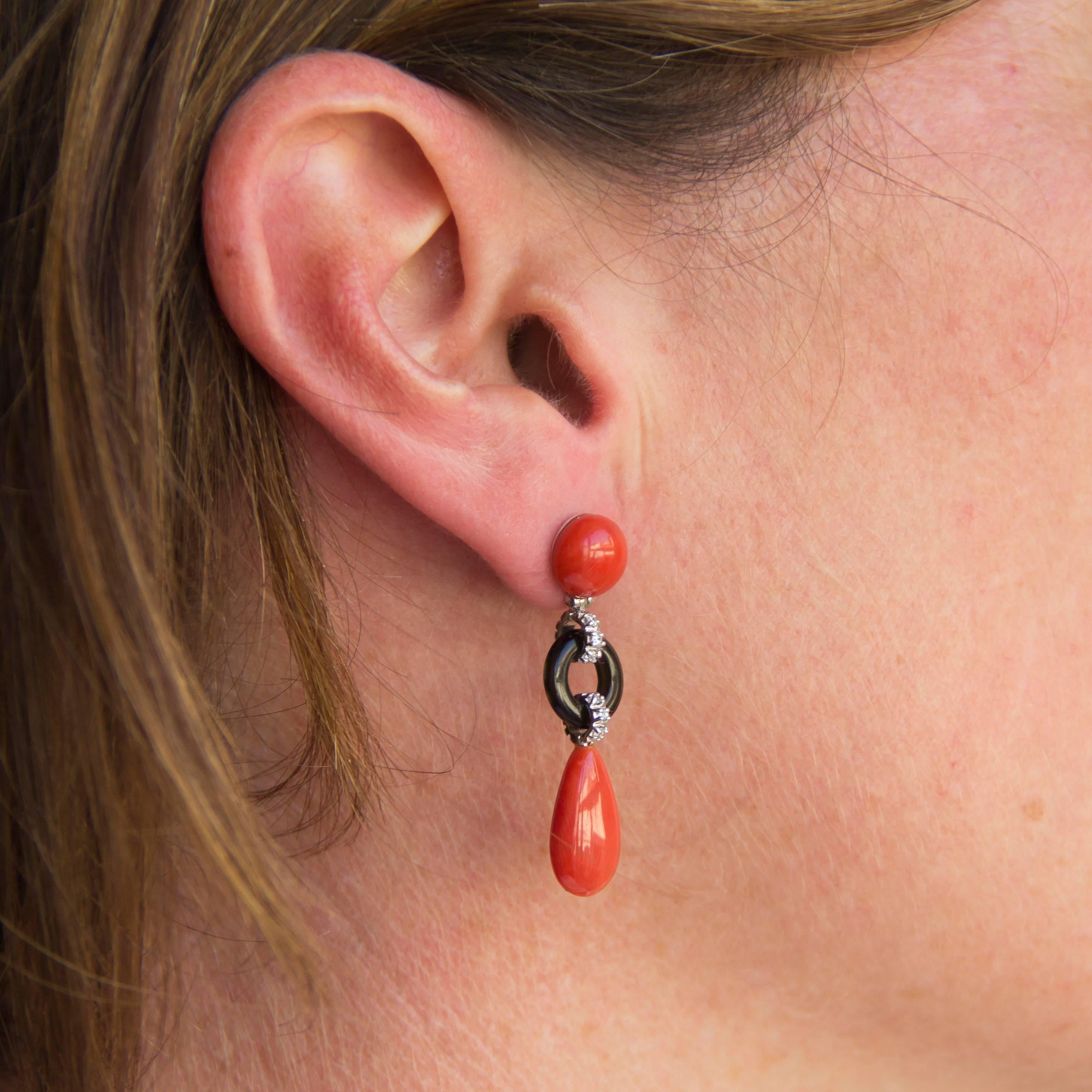 Earrings in 18 Karats white gold.
Delightful dangle earring, each gold earring is composed of a Mediterranean cabochon coral which holds in pendulum a curved disc of onyx set with a line of brilliant cut diamonds itself retaining a drop of coral.