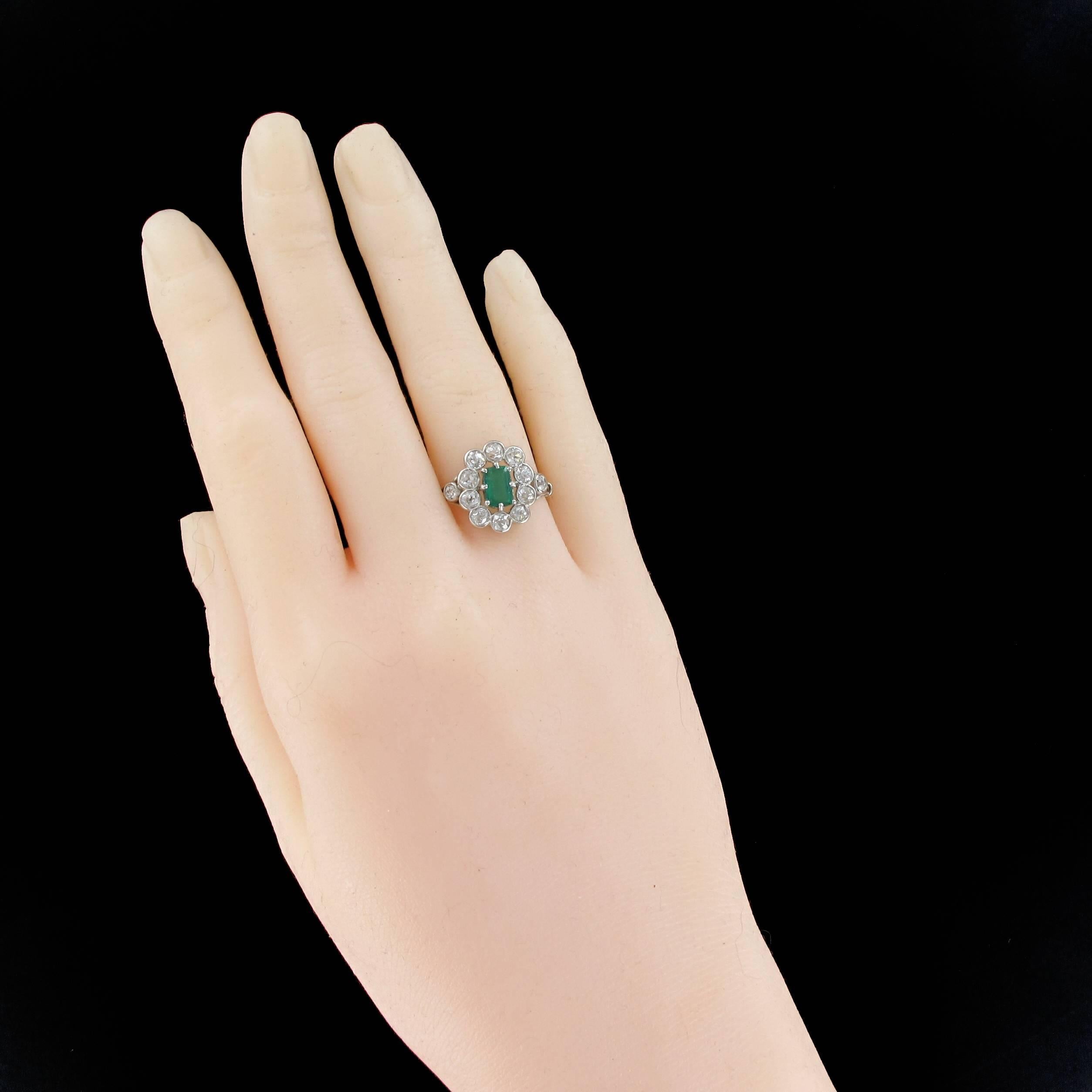 Ring in 18 carats white gold. 

Absolutely splendid, this antique ring is set with 8 claws on its top of an intense green emerald surrounded by 10 antique brilliant cut diamonds in millegrains set. On either side, another diamond is set on the start