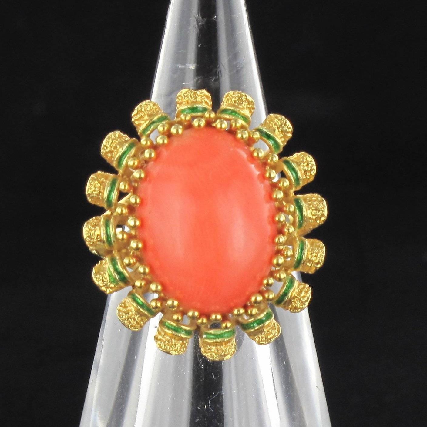 Ring in 18K yellow gold, owl hallmark.
This ring is set with a coral cabochon held by beaded claws. Bordered by chiselled and green enamelled gold convex petals. The bed and shoulders of the ring are pierced style openwork.
 Height: 2.4 cm, width: