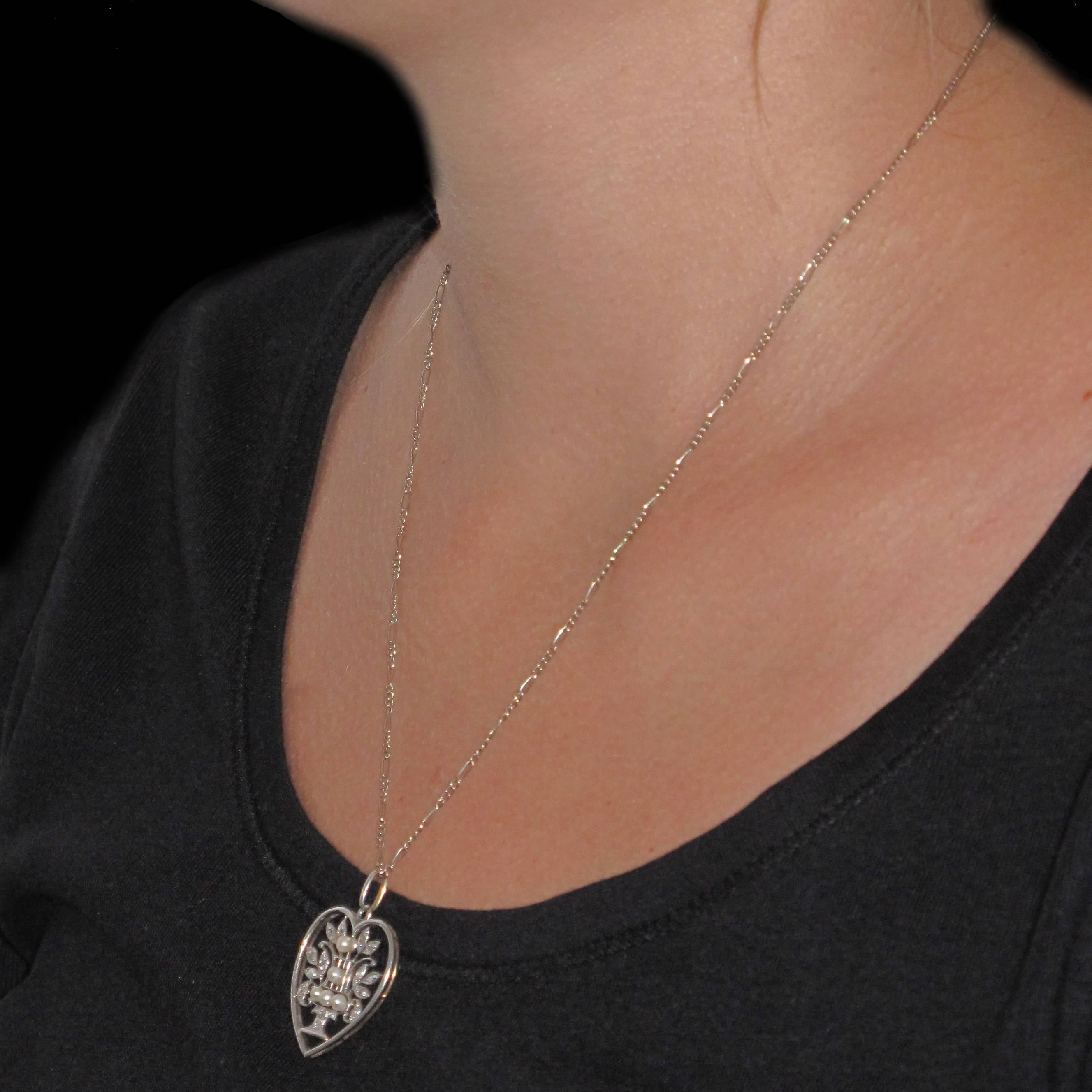 Pendant and chain in 18 carat white gold, eagle head hallmark. 
In the form of a heart, the openwork design features a vase or goblet set with fine pearls and diamonds surrounded by leaves set with diamonds. The pendant is on a curb chain. 
Chain