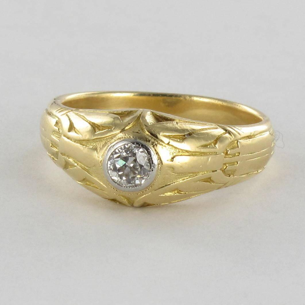 Ring in 18 carat yellow gold. 

A men’s gold signet ring, featuring a bezel set antique brilliant cut diamond of excellent quality set in white gold. The ring band is engraved over half of its surface with geometric forms around the central