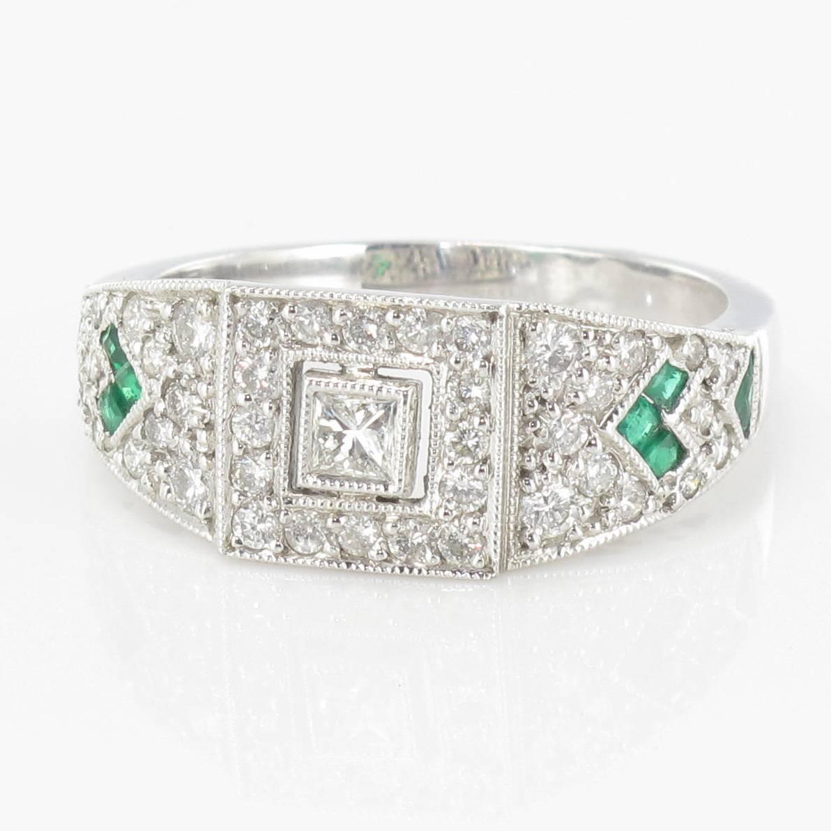 Ring in 18 carat white gold, eagle head hallmark. 

Set with a central princess cut bezel set diamond with a brilliant cut diamond surround, set on each side with diamonds and emeralds. 

Total diamond weight: about 0.50 carat 
Total emeralds
