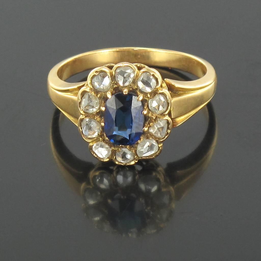 Ring in 18 carat yellow gold, eagle head hallmark. 

This daisy ring features a claw set central oval blue sapphire encircled by 10 bezel set diamonds. 

Height: 1.3 cm, width: 1.1 cm, thicness of the ring: 2.1 mm
Total weight of the jewel: