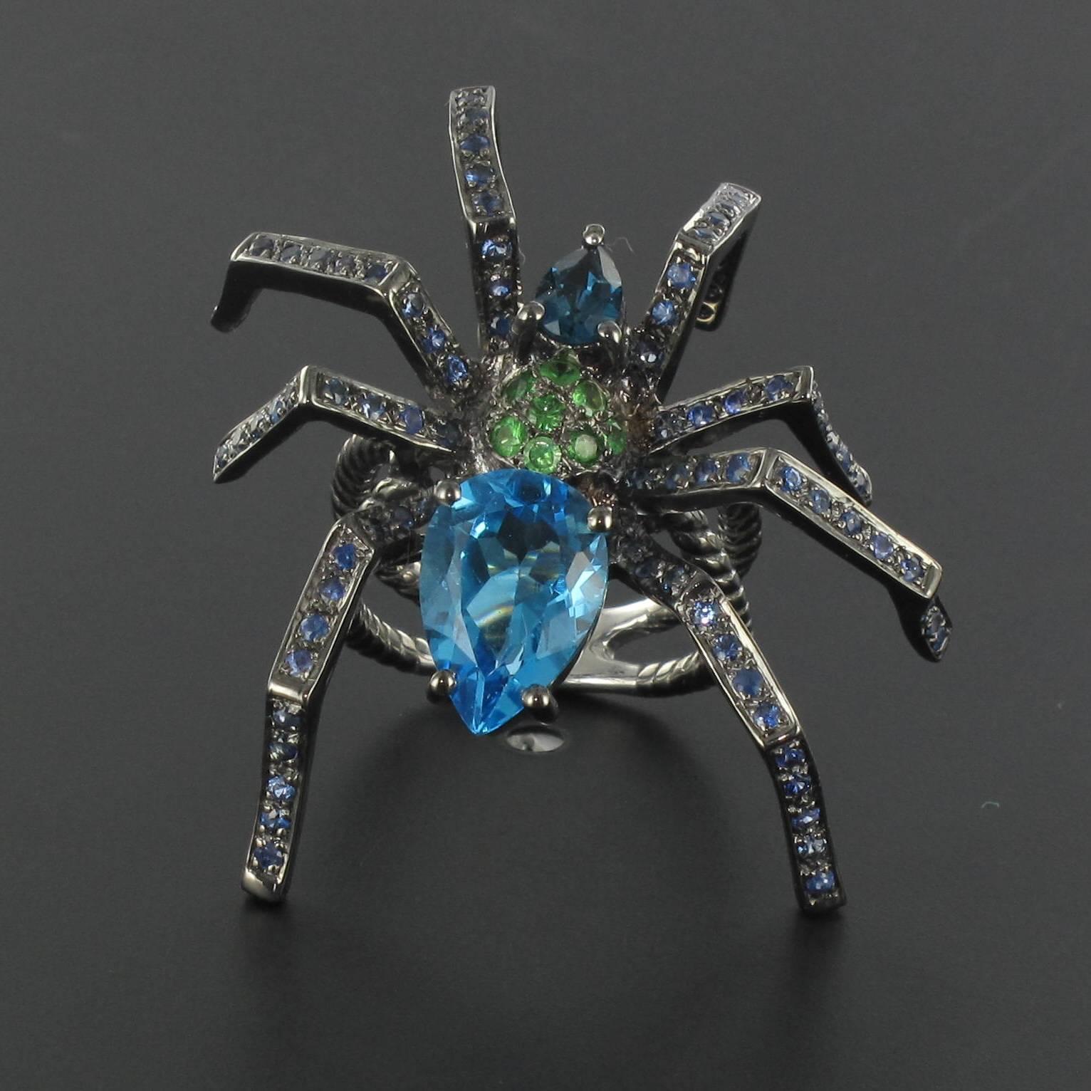 Silver Ring with black rhodium.

This incredible black silver ring is in the realistic form of a spider. The body of the spider is composed of 2 pear cut topazes with a pave of 9 round tsavorite green garnets. The legs are set with round