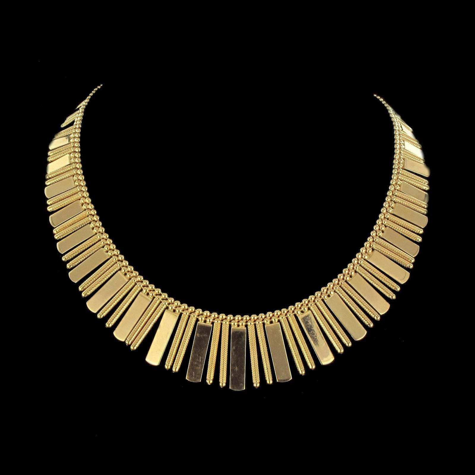 Necklace in 18 carat yellow gold. 
Composed of a double row of golden beads supporting a design formed of sets of 2 golden bars separated by golden beads holding flat gold plates chiselled on the front and smooth at the back. The clasp is a safety 8