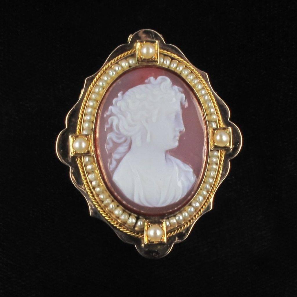Pendant - brooch in 18 carat yellow gold. 

This pendant necklace features a cameo in agate of a woman’s profile with raised hair surrounded by fine pearls and edged with a fine twisted gold border. At each of the cardinal points is a larger fine