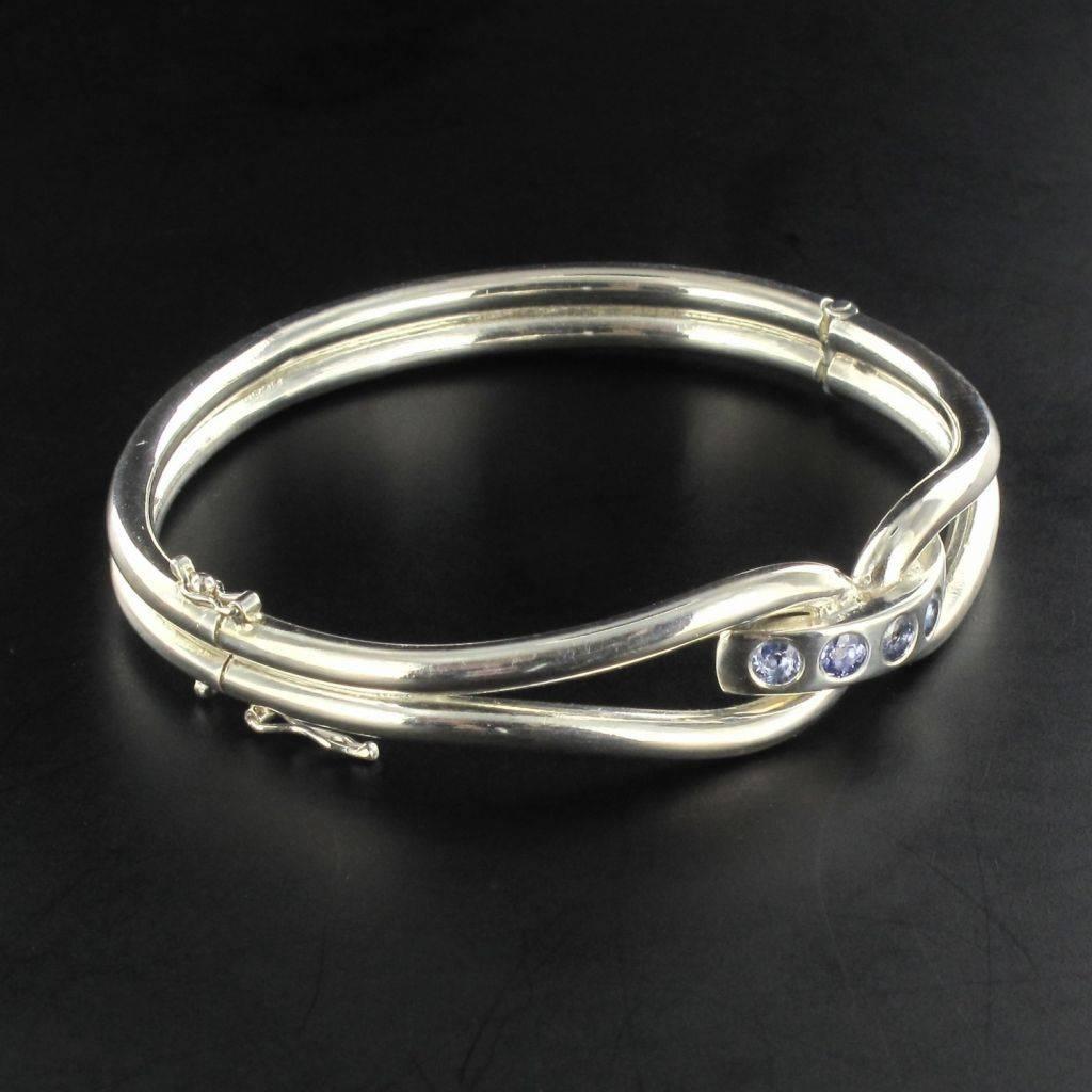 Silver Bracelet 925.

This lovely bracelet is composed of 2 bangles connected by a curved link set with a line of sapphires. It opens at the side with a hinge. The clasp features 2 safety 8 fixtures. 

Total weight of sapphires 1.03 carat