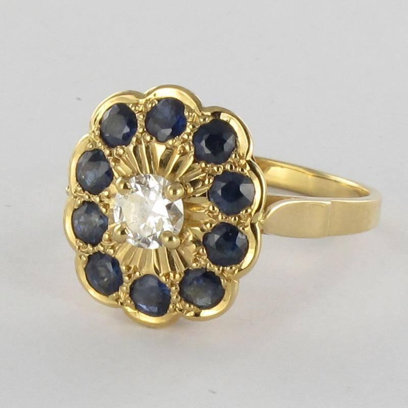 Ring in 18 carat yellow gold, eagle head hallmark. 

This yellow gold ring is claw set with a central brilliant cut diamond surrounded by a multilobed chiselled bed set with 10 round sapphires. 

Height: 1.58 cm, width: 1.38 cm, ring width at