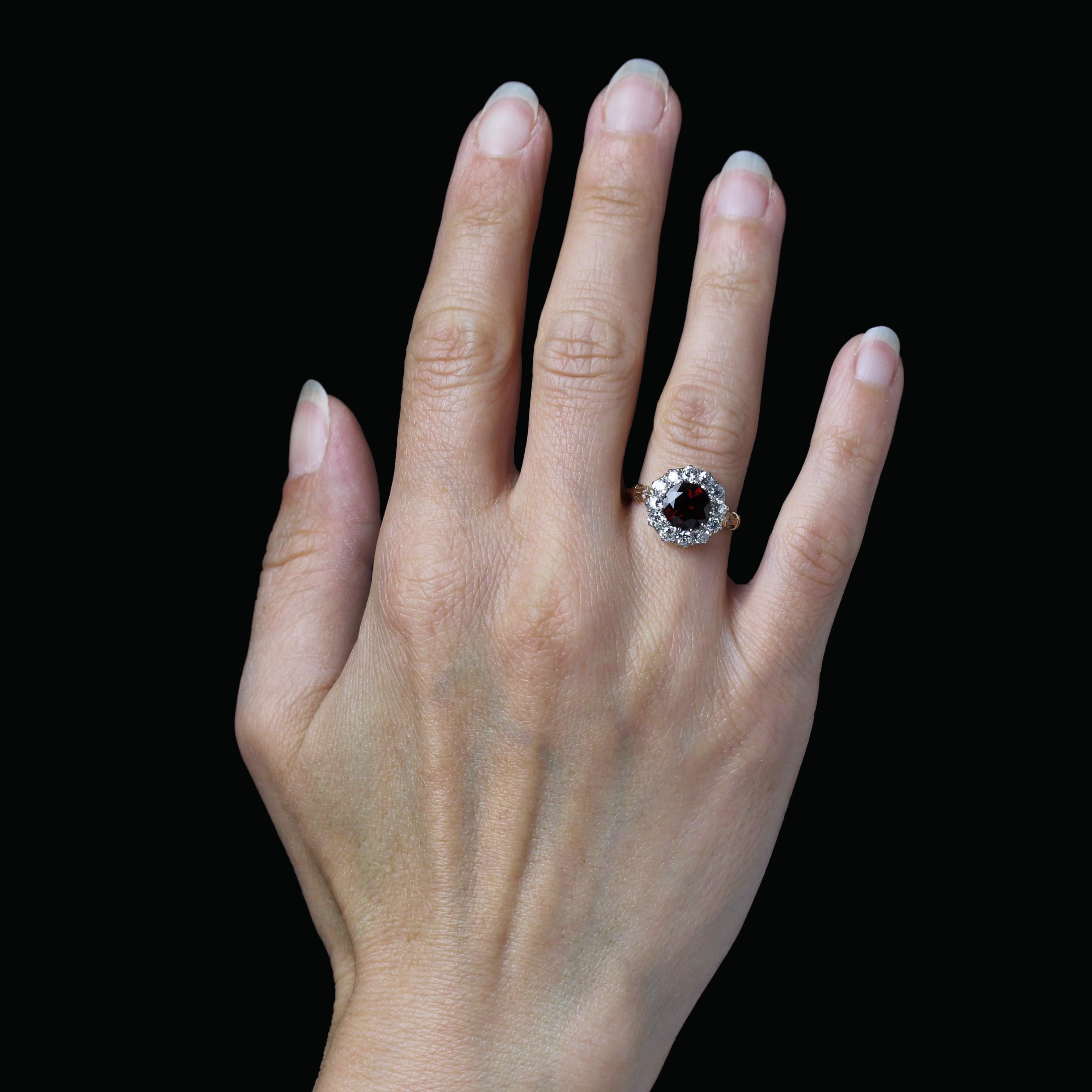 Bague en or jaune 18 carats et en platine.
Cette sublime bague ancienne de forme ronde est ornée d'un halo de diamants taillés en brillant et d'un grenat rhodolite rond et facetté. De chaque côté de la tête, le début de l'anneau est orné d'un petit