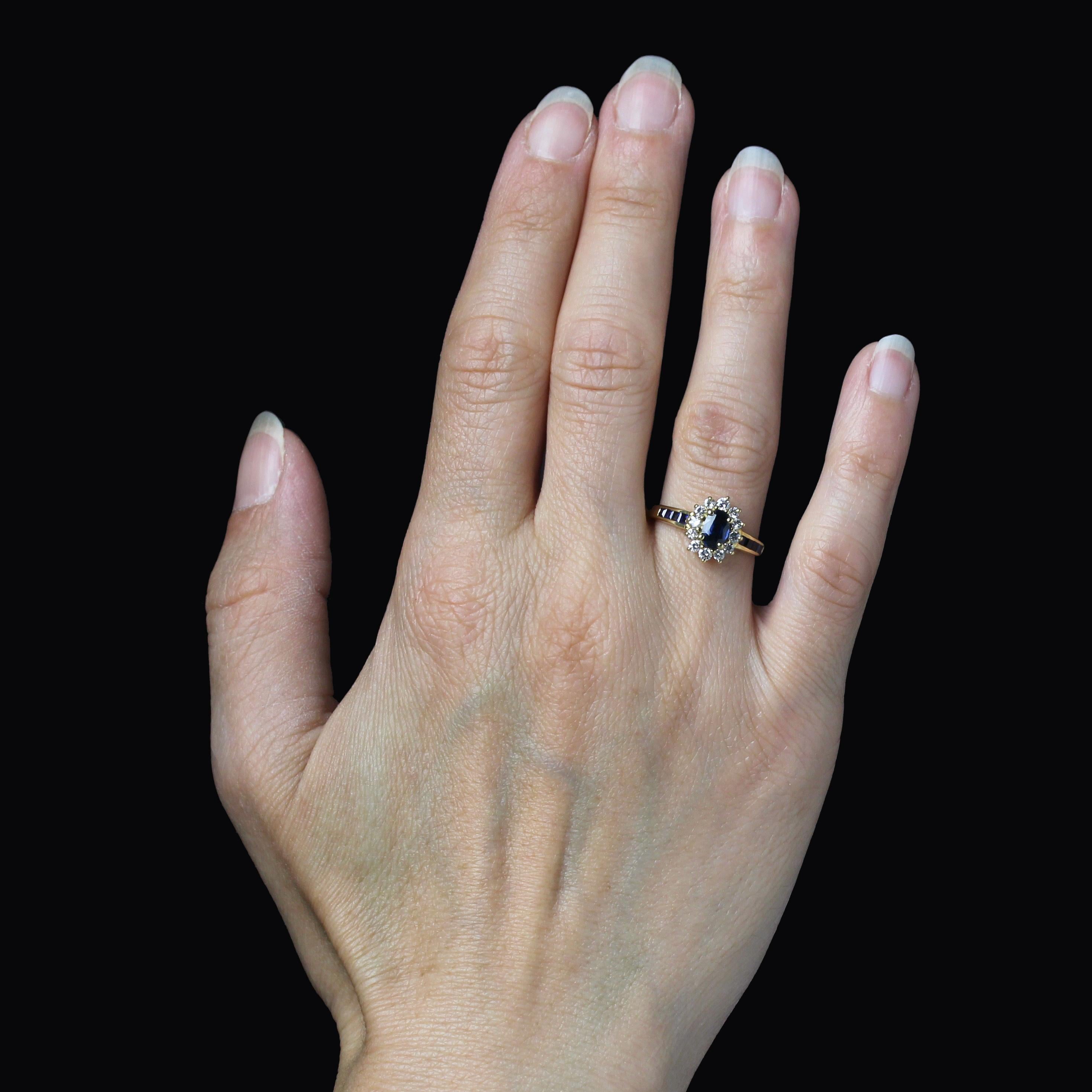 Bague en or jaune 18 carats.
Ravissante bague d'occasion en or jaune, sertie en forme de marguerite, avec un saphir ovale retenu par 4 griffes au cœur et des diamants modernes de taille brillant entourant les pétales. La corbeille est ajourée et le