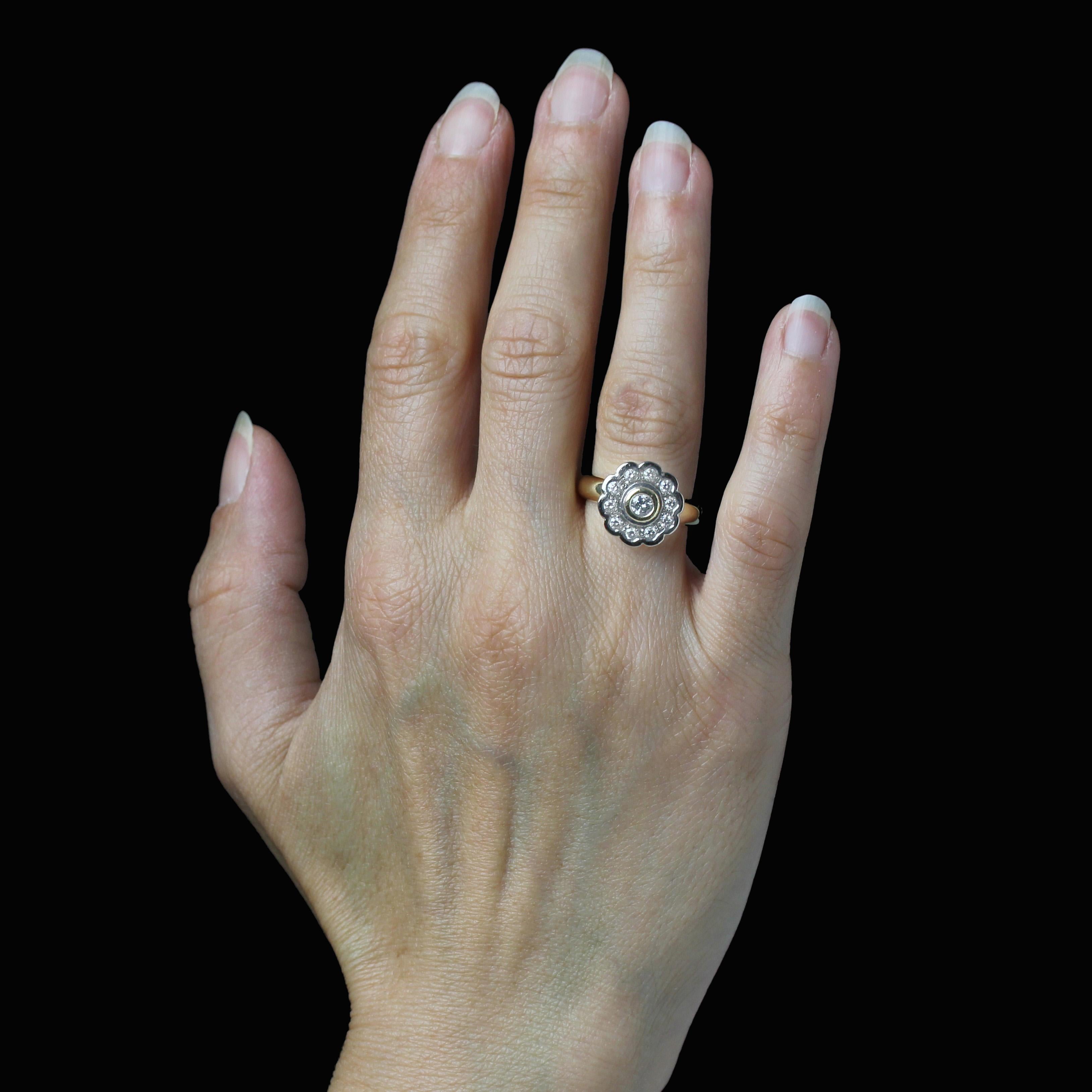 Whiting en or jaune et blanc 18 carats.
La monture de cette bague d'occasion en diamant est en forme de fleur. Un diamant moderne de taille brillant est serti au centre et entouré de 9 diamants modernes de taille brillant dans le motif de la fleur.