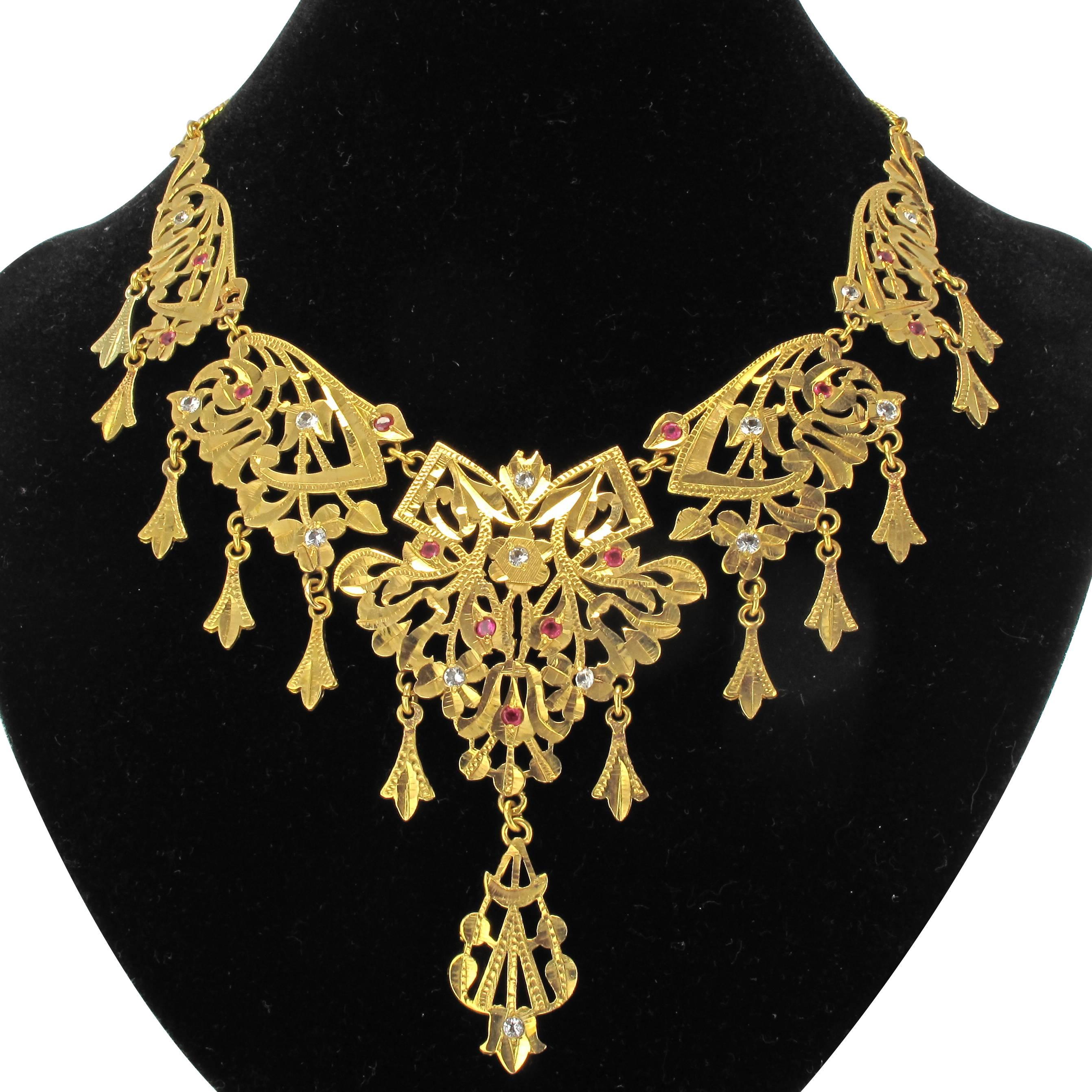 18 carat yellow gold necklace.
An imposing antique necklace formed of 5 finely engraved articulated gold plates with arabesque openwork and leafy motifs. The design is set with small white sapphires and red gems. The necklace is completed with