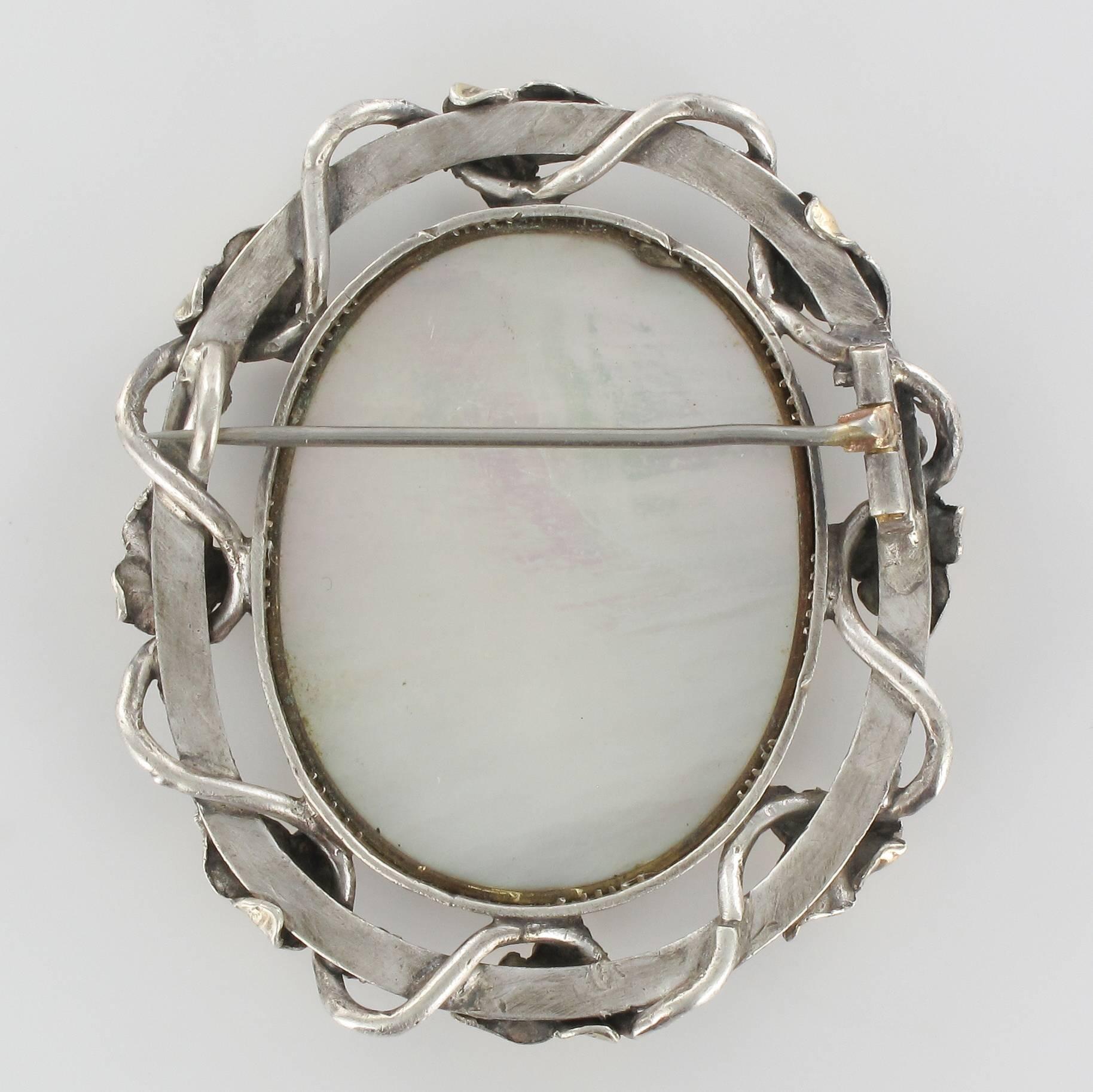 Brooch in silver and 18 carats yellow gold.
This rare antique memory brooch is composed of an oval motif made of braided hair on a mother-of-pearl tablet set with initials and protected by a glass. The whole is surrounded by a vegetable decoration