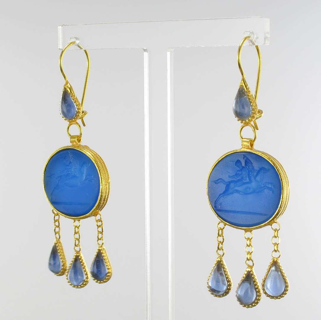 For pierced ears.

Pair of earrings in vermeil, silver and yellow gold.

Drop earrings are set by a blue intaglio on glass paste and glass crystals. The clasps are goosenecks with safety hooks. 

Overall length: 6.5 cm, width to the widest: 2 cm,