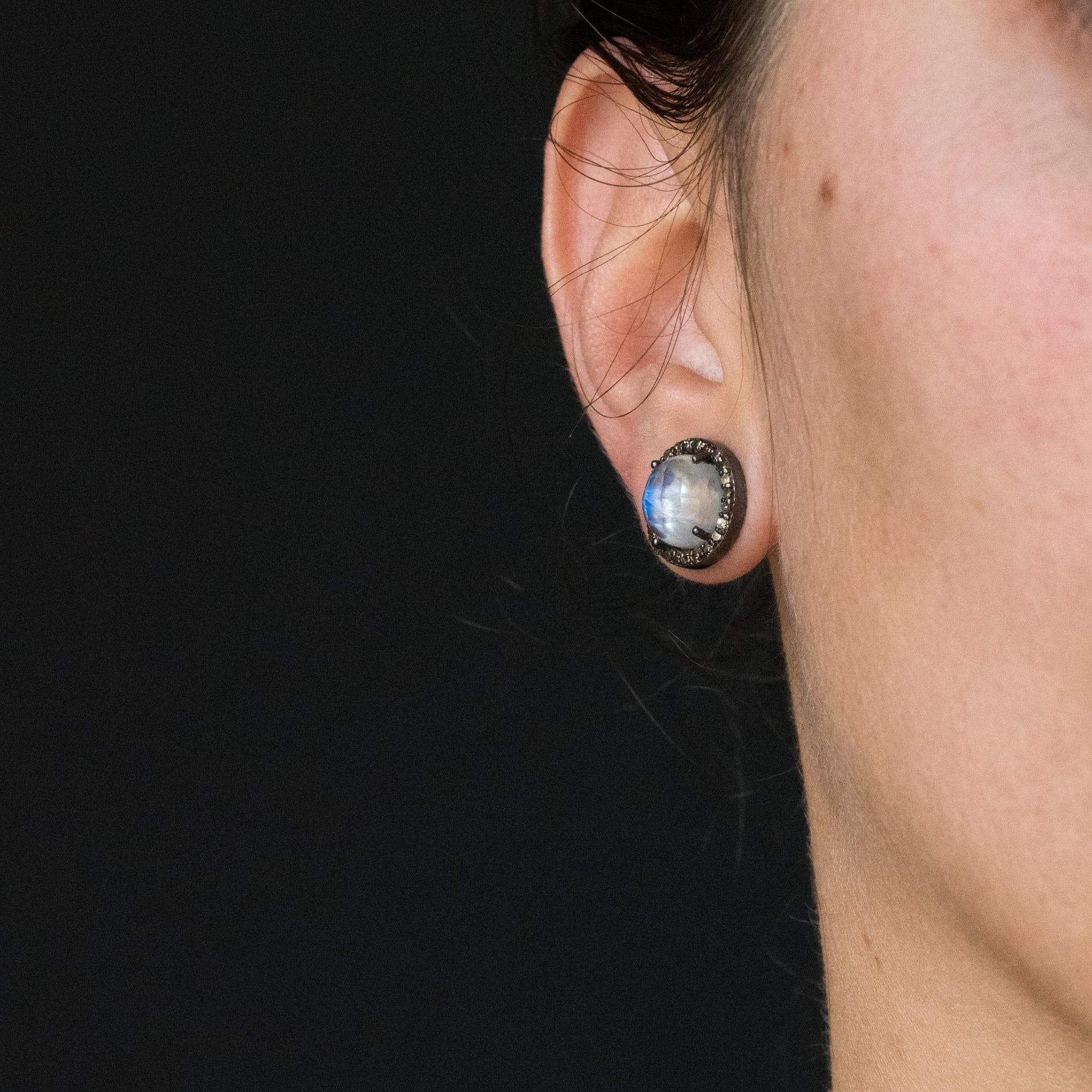 Pair of ear studs in silver, black rhodium.
Beautiful and round, each earring is set with a faceted moonstone surrounded by brilliant- cut diamonds. The closure system is a nail with butterfly.
Height: 1.2 cm, thickness: 5.5 mm.
Total weight of the