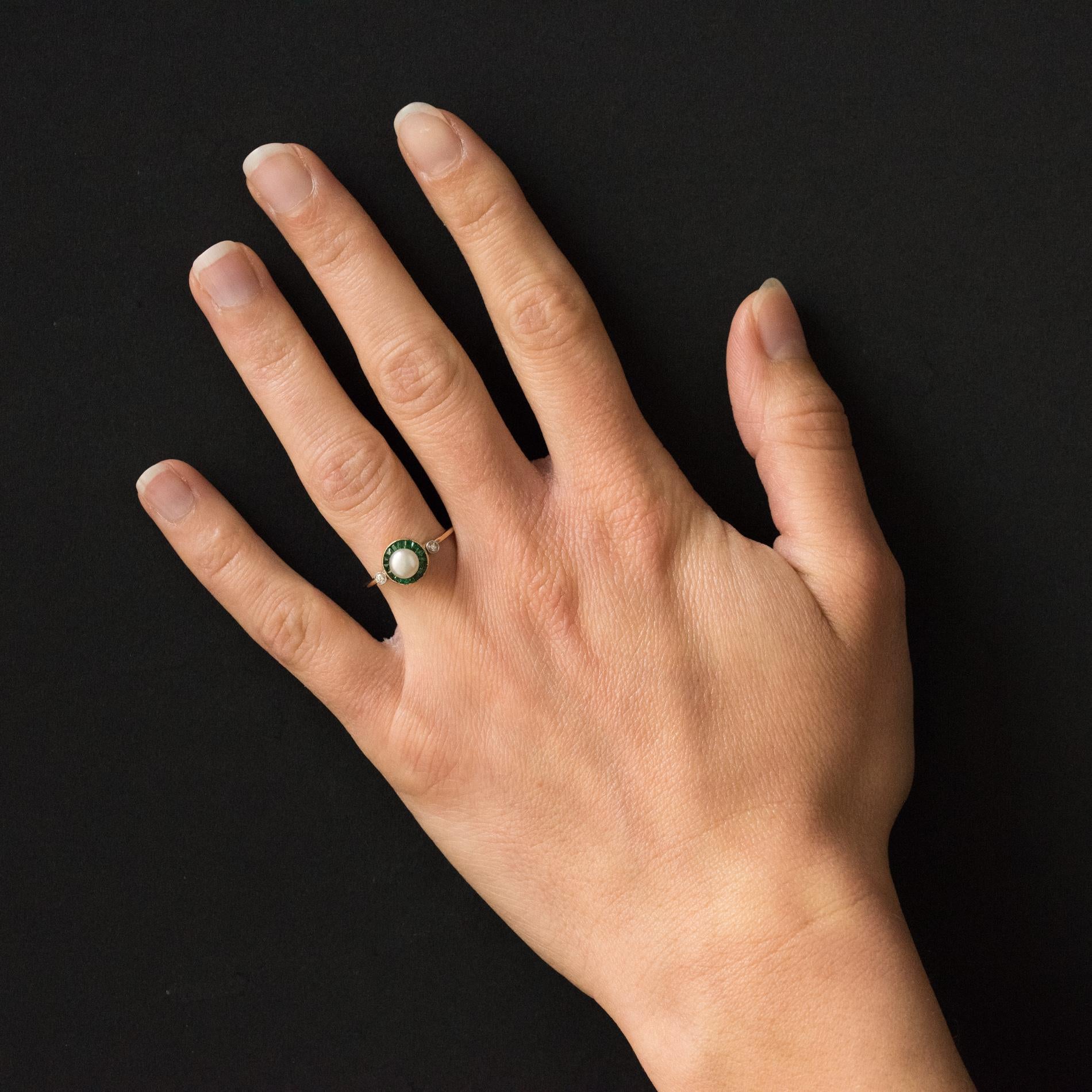 Ring in 18 karats yellow gold, eagle's head hallmark.
Lovely antique jewel, its round tray is set with a button natural pearl in an entourage of calibrated emeralds. On either side, on the start of the ring are beaded closed set 2 x 1 brilliant- cut