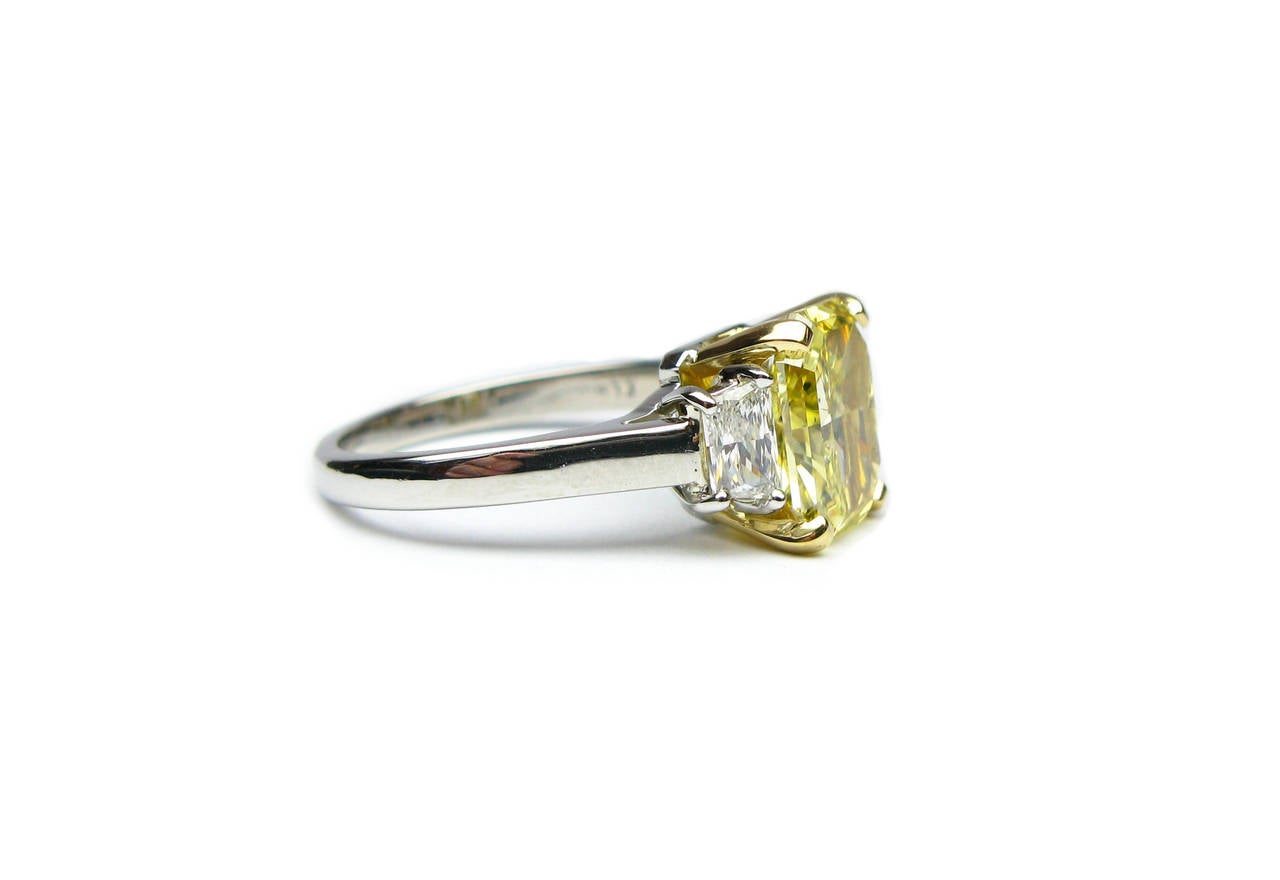 This show stopping 2.52 carat fancy vivid yellow  radiant diamond ring is set in a lovely platinum and 18kt yellow gold ring. The yellow diamond is set in between two 0.46ctw diamond trapezoids. This ring is a stunning piece every girl dreams to