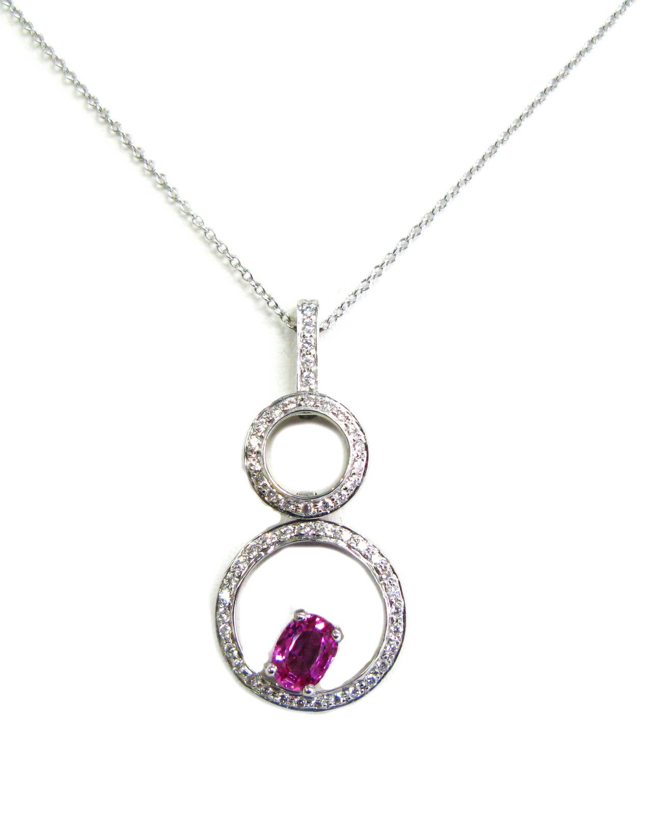 This fashionable 18kt white gold pendant is part of the Kurt Wayne collection. This piece features two pave set diamond circles with 0.40ctw round brilliants and an oval cut pink sapphire gemstone weighing 0.92cts suspended from an open link chain.