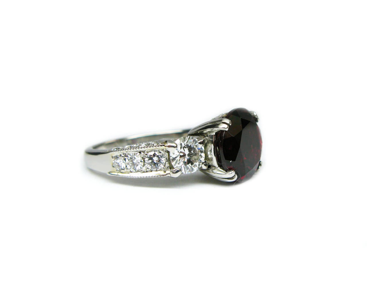 This unique platinum cocktail ring is comprised of prong set round brilliant diamonds graduating in size down the side of the band with pave diamond accents along both the top and bottom. The center stone is a stunning 4.57ct round rhodolite garnet