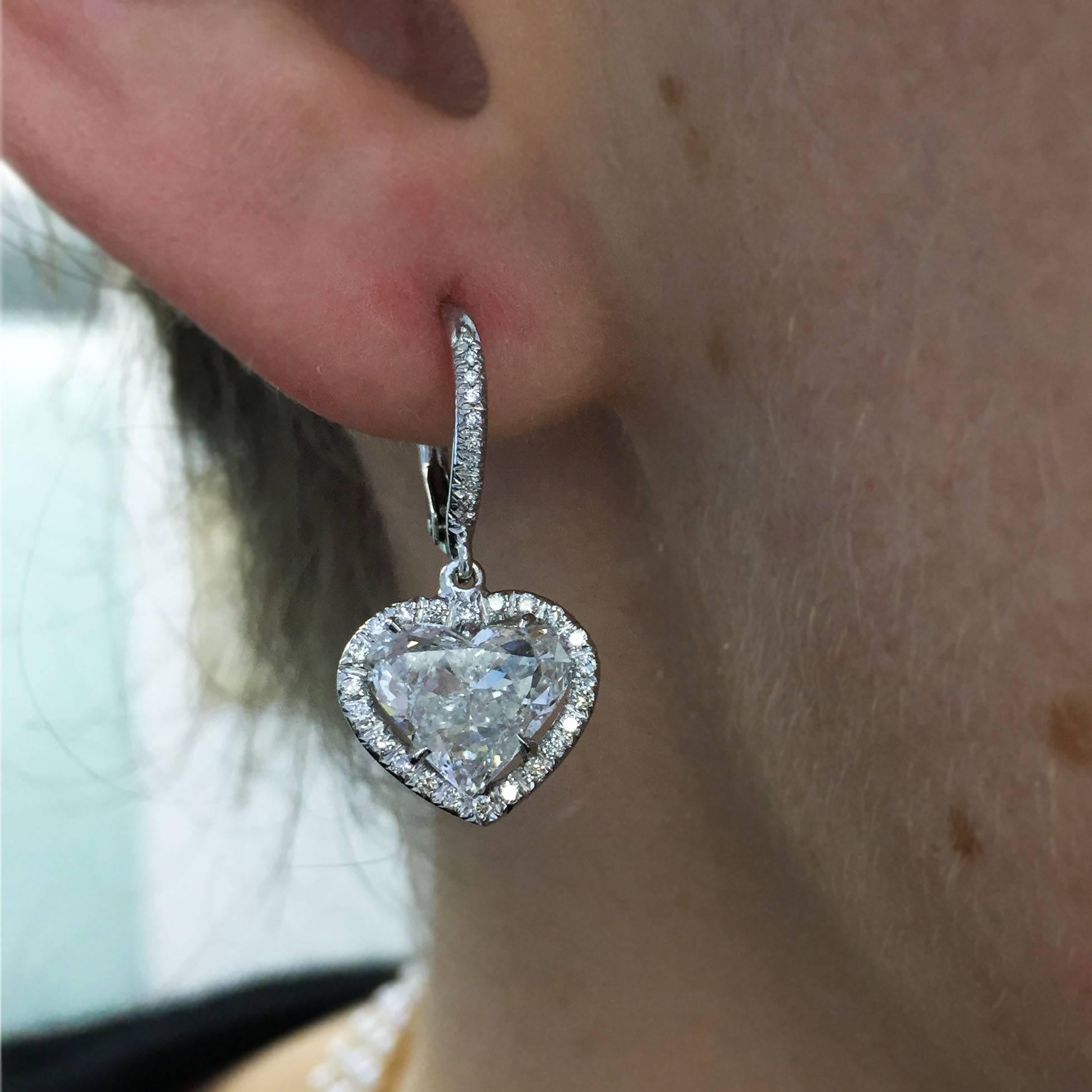 The perfect gift for your Valentine! A sweet pair of 18k white gold earrings features two heart-shaped diamonds prong set in a pave halo frame and suspended from a pave wire. The diamonds weigh 1.70 carats and 1.81 carats, while the earrings are set