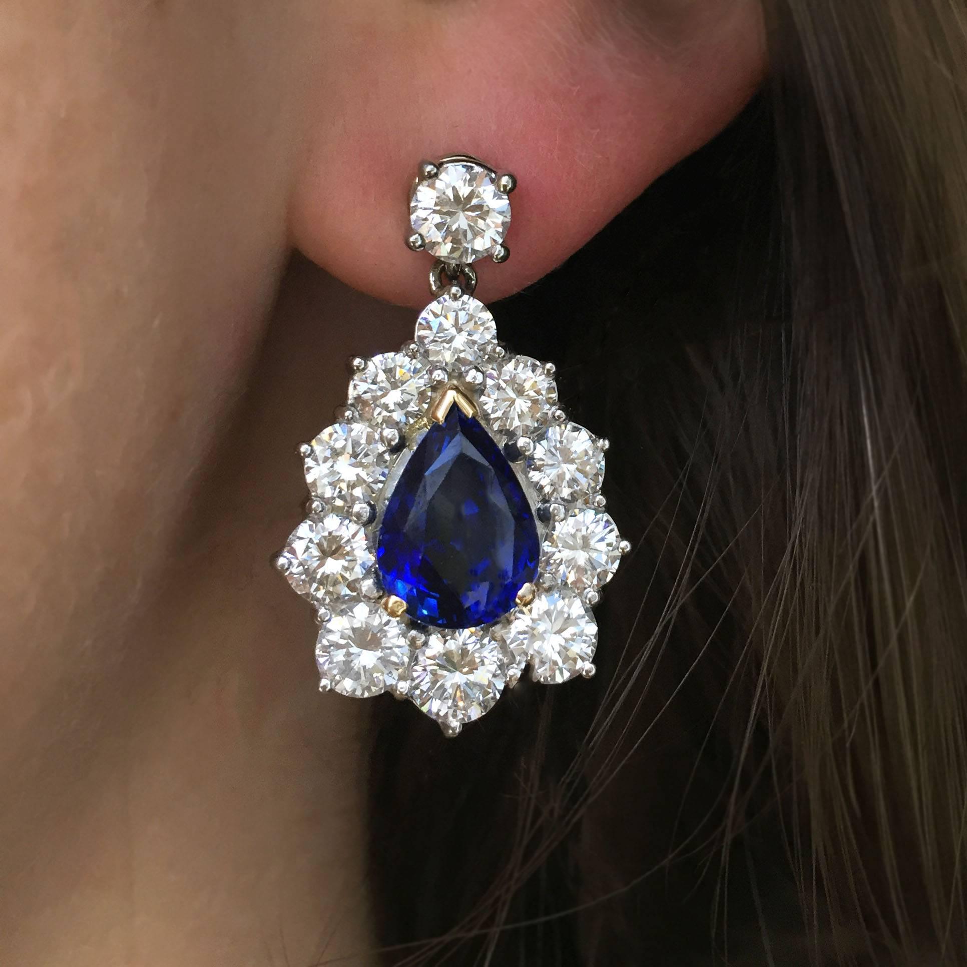 This stunning pair of earrings features two GIA-graded pear-shaped royal blue sapphires, 8.14 carats total, in diamond surrounds, suspended from single round diamonds. Mounted in 18k white and yellow gold, these earrings contain 22 round