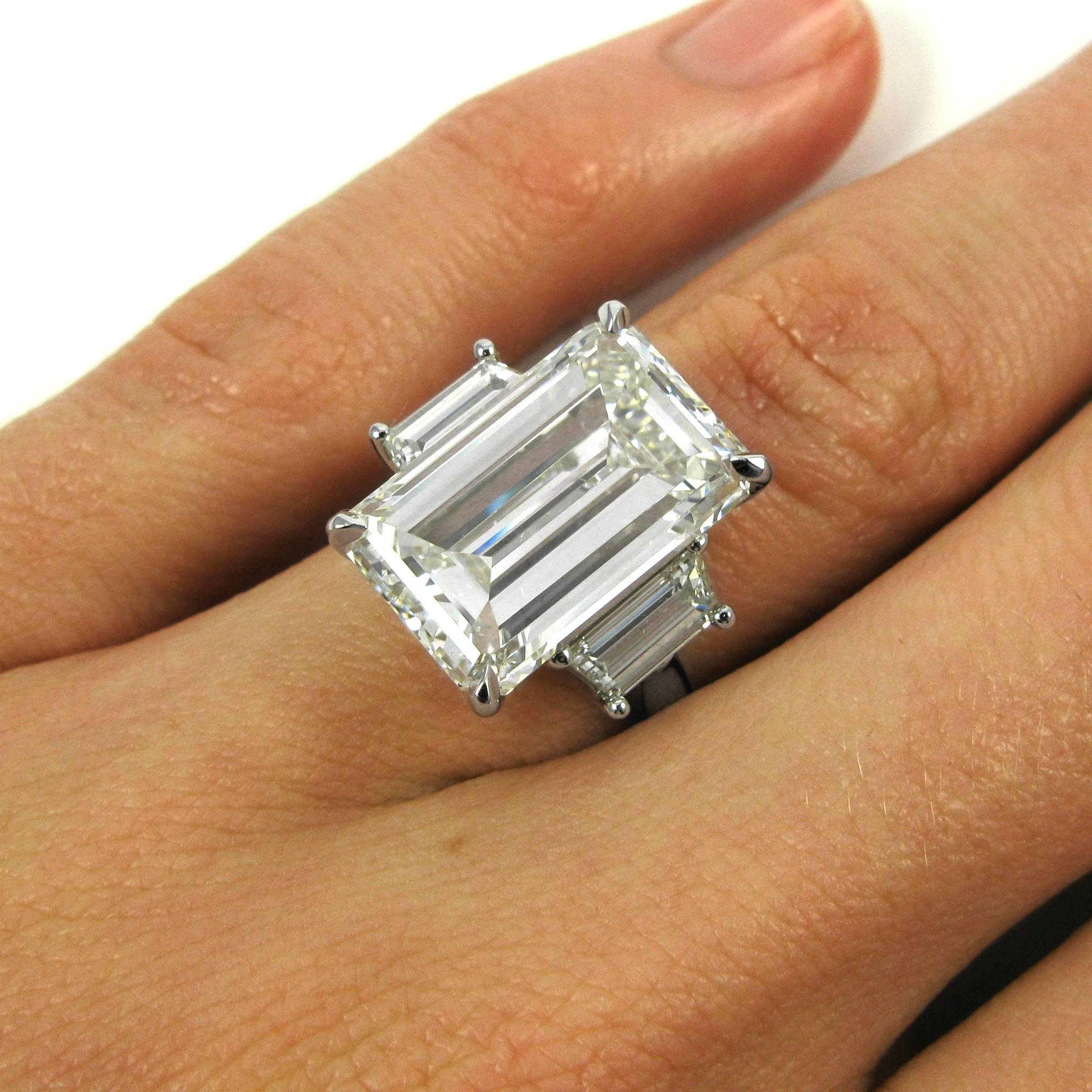 A lovely ring centering on a 10.38 carat emerald-cut diamond with J color and SI1 clarity, flanked by two trapezoid-cut diamonds totaling 1.08 carats. The three diamonds are set in four-prong basket settings atop a plain platinum ring shank.