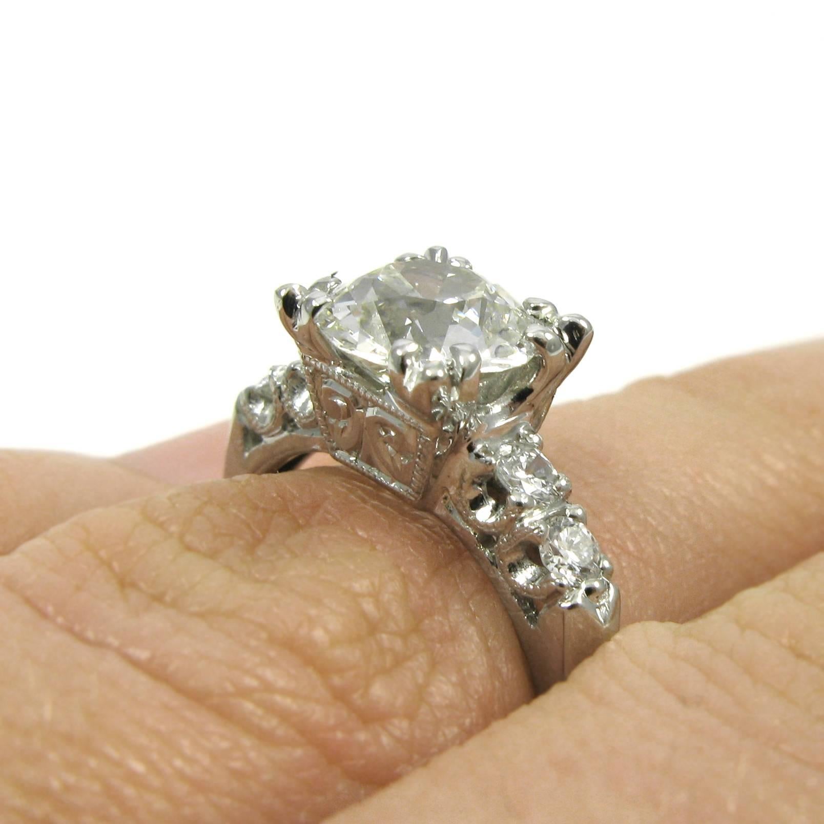 A lovely 18k white gold engagement ring featuring a 1.41 carat Old European-cut diamond with L color and SI1 clarity. The diamond is set in an engraved box setting with trefoil prongs accented by diamond-set shoulders with milgrained fishtail
