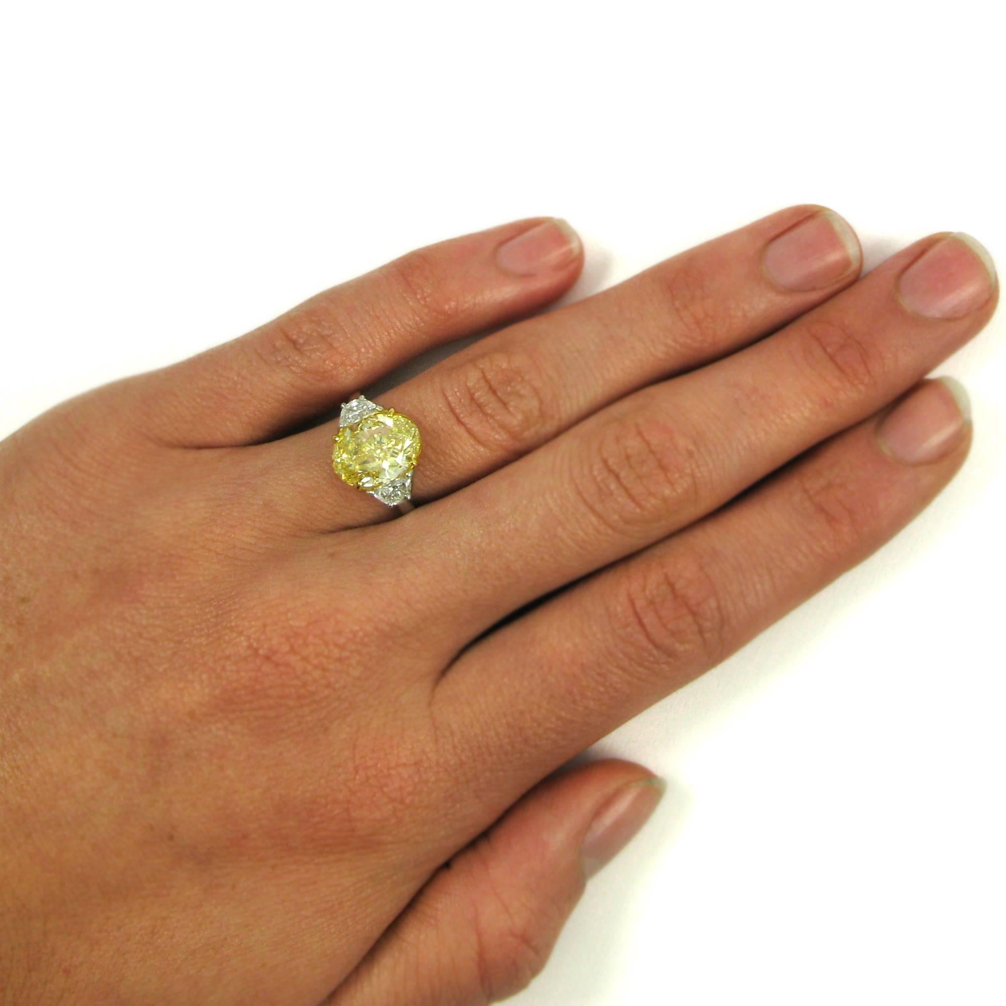 A lovely three-stone ring centering on a bright and cheerful Fancy Intense Yellow oval-cut diamond with VVS1 clarity. The yellow diamond is prong-set in 18k yellow gold, and is flanked by two white half-moon diamonds totaling approx. 0.70 carat.