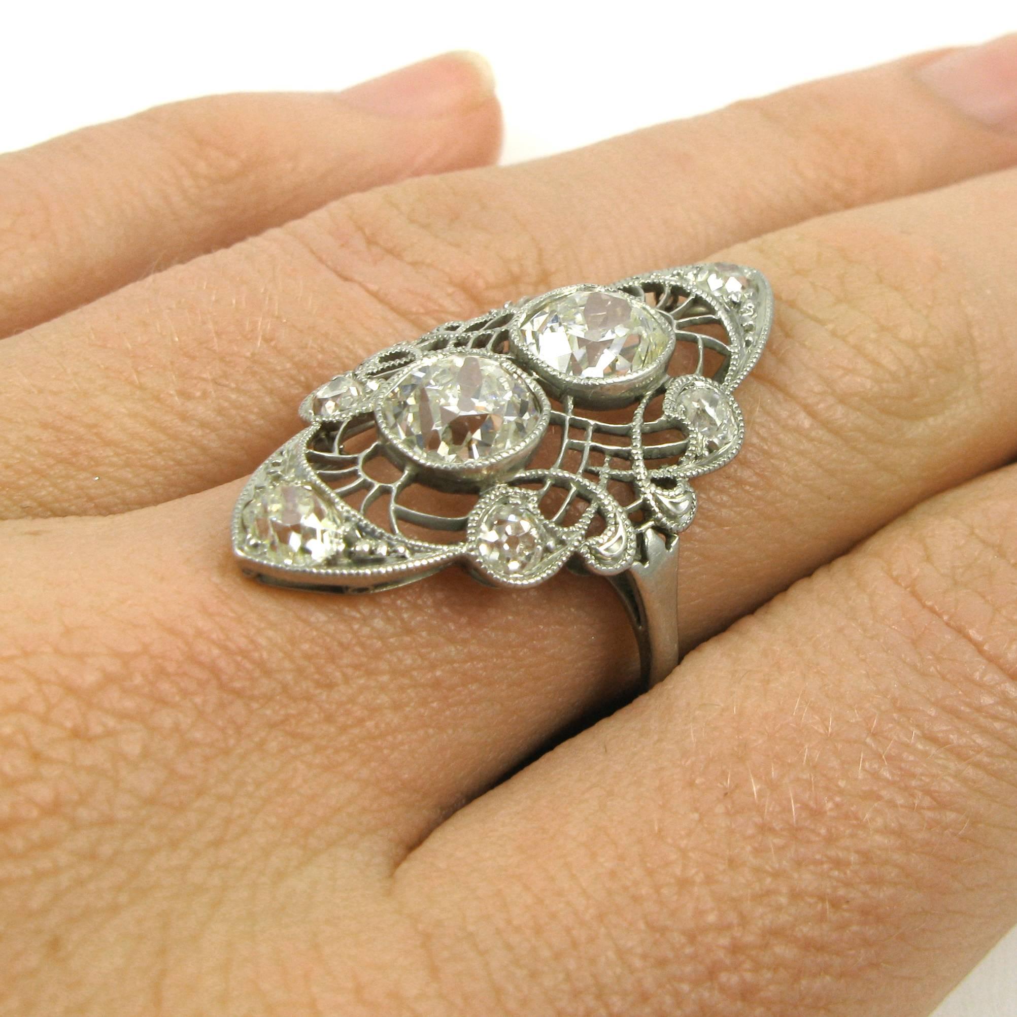 A lovely vintage piece featuring eight Old Mine-cut diamonds of various sizes set in an elaborately filigreed dinner style mounting atop a thin ring shank. Platinum, with delicate wirework and milgrain accents. 
