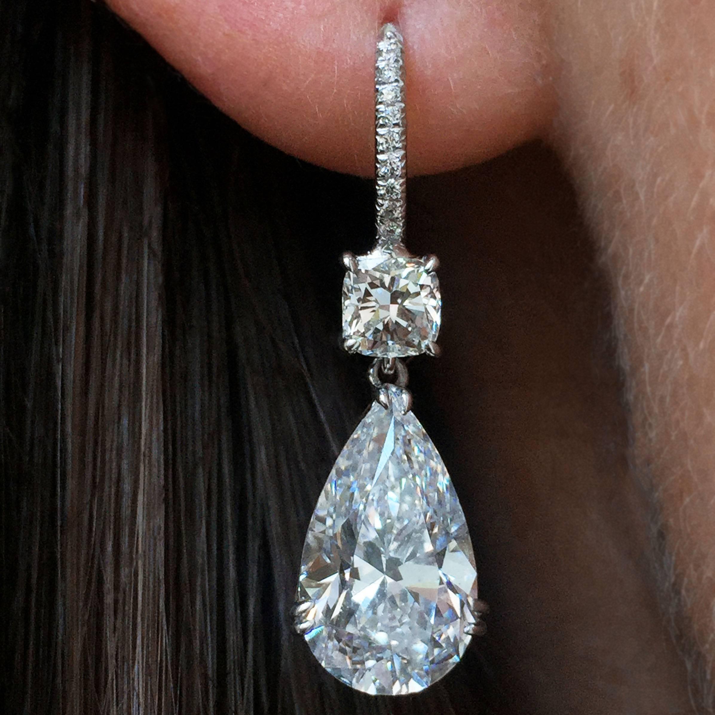 A stunning pair of elegant 18k white gold drop earrings composed of two cushion-cut diamonds on pave wires suspending lovely 3 carat D color pear shape diamond pendants designed by J. Birnbach.  The two cushions weigh 0.81 carat total, with an