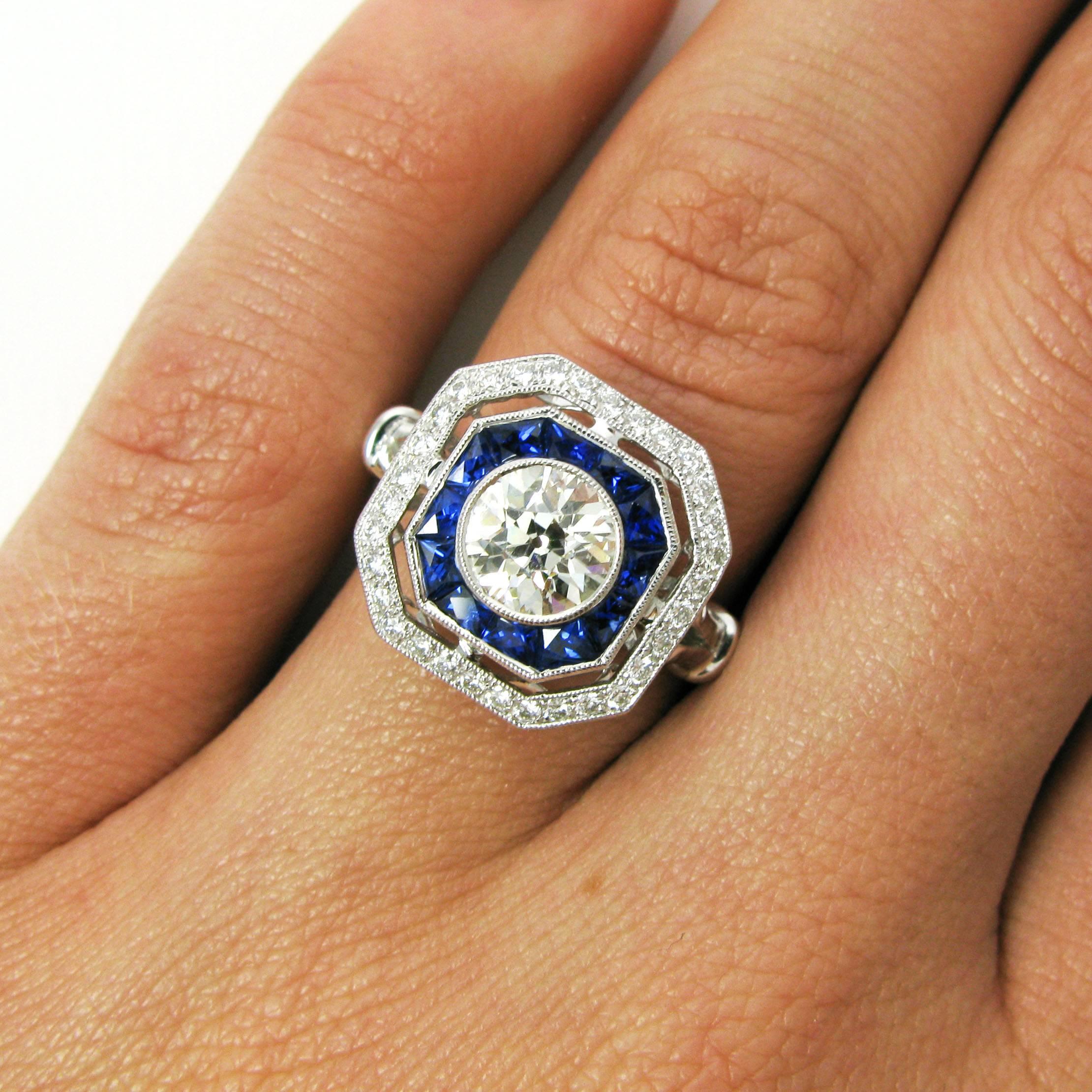 This lovely vintage-inspired ring features a 1.03 carat Old European-cut diamond bezel set into a custom calibre cut sapphire frame surrounded by a pave diamond frame. Set low on a split shank with an elaborate gallery and pierced and milgrain