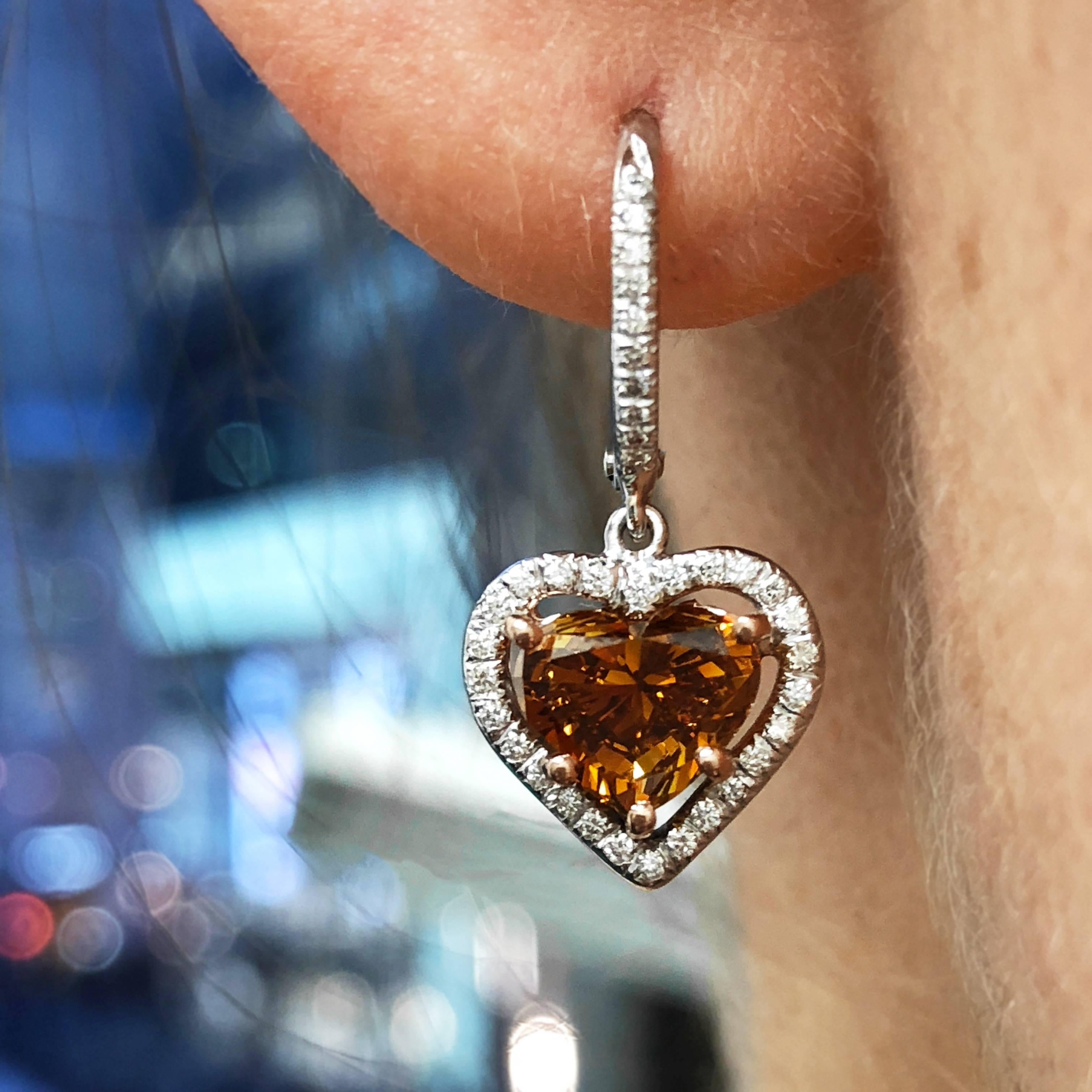 Special earrings for your special someone! These unusual drop earrings feature a matched pair of Fancy Deep Orange heart shape diamonds set in rose gold in custom 18k white gold pave halo frames. The heart shapes weigh 1.23 carat and 1.08 carat