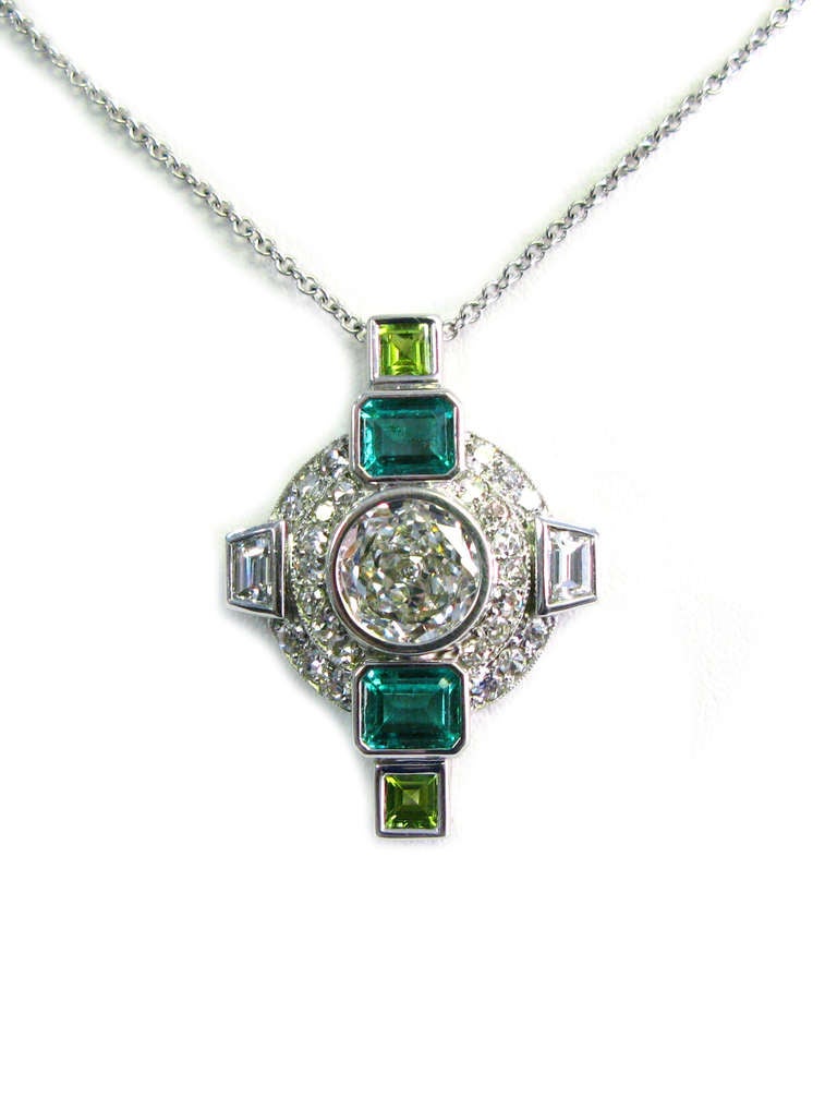 This Neiman Marcus signed 18kt white gold pendant features an approximately sized 2.50-3.00 carat round brilliant bezel set center diamond surrounded by 13 round brilliant diamonds, 2 diamond traps, 2 step-cut emeralds and 2 step-cut peridots. This