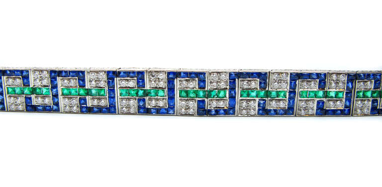 Diamond Emerald Sapphire  platinum bracelet features a geometric weaving pattern of French cut deep blue sapphires that are complimented by lovely French cut emeralds and round brilliant diamonds. This incredible piece is one that is sure to take