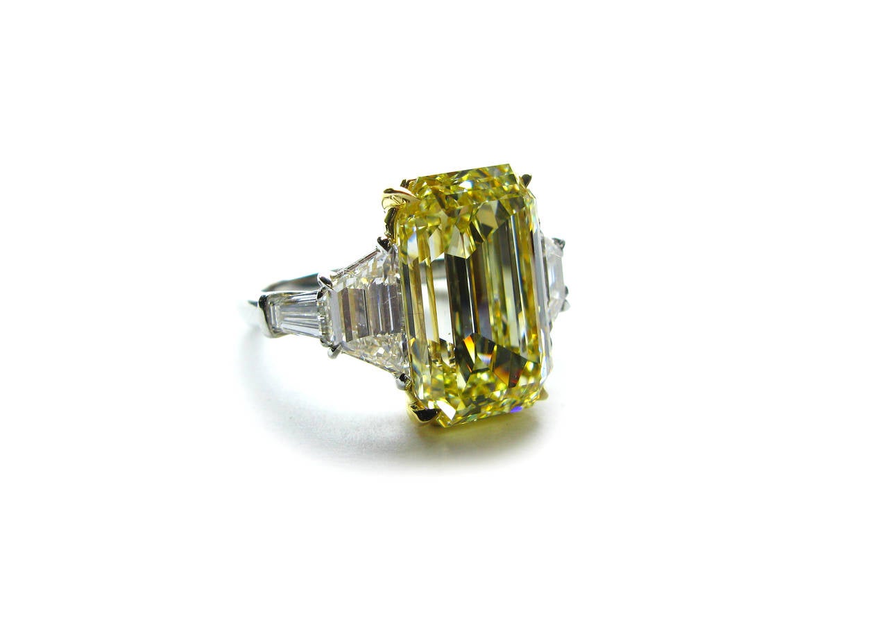 This stunning handmade platinum and 18kt yellow gold ring features a rare GIA certified 8.25ct, Fancy Yellow color, VS1 clarity, Emerald cut diamond with 1.54ctw trapezoid diamond and 0.60ctw tapered baguette diamond sidestones. This piece is meant