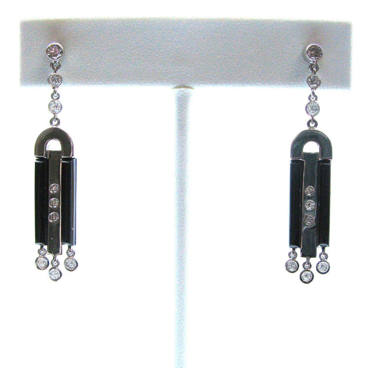 Uniquely designed diamond and onyx earrings in a distinct art deco style.  These 18kt white gold dangle earrings feature 12 H/I color, VS clarity round brilliant bezel set diamonds and 6 flush set diamonds and 4 onyx baguettes.