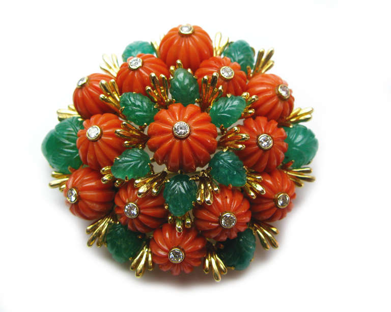 This David Webb signed pin creates a bouquet featuring floral like coral pieces with round brilliant diamond centers and lovely green emeralds carved in a leaf like design, all set in 18 karat yellow gold. This whimsical piece is a fun way to add a