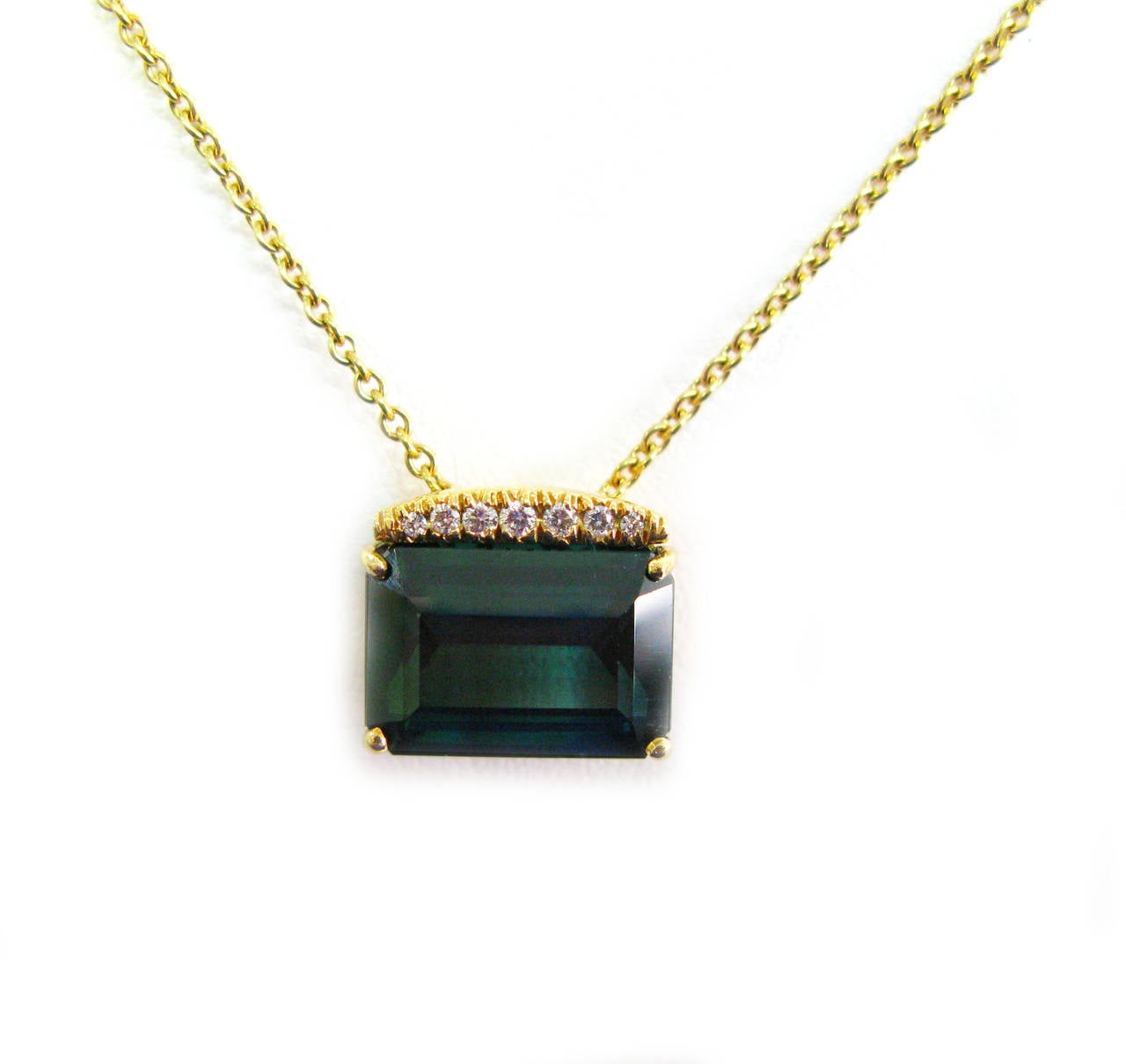 This beautiful 18kt yellow gold Kurt Wayne signed pendant features a stunning deep bluish green step cut tourmaline weighing 7.22cts with a row of 7 graduating prong-set round brilliant diamonds totaling 0.08cts suspended from a 16