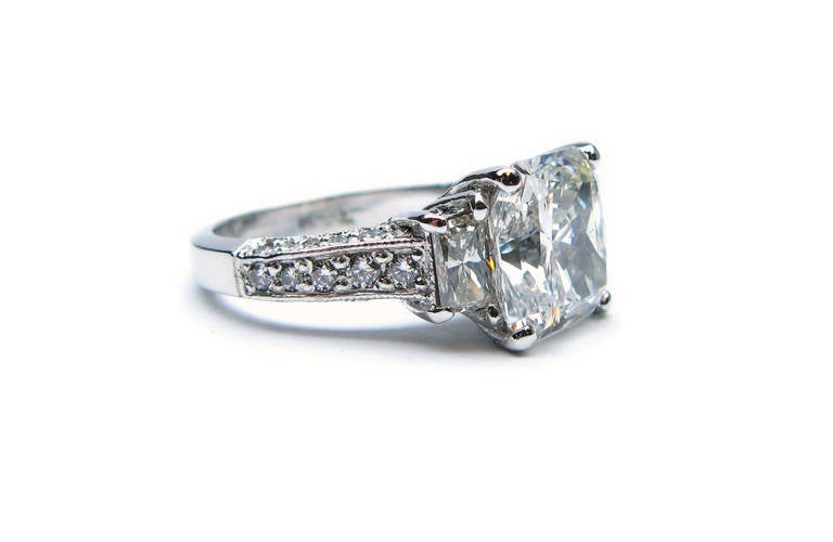 This GIA certified 3.88 carat E color VS1 clarity radiant cut diamond is set in a lovely platinum ring with two diamond trapezoids and round brilliant diamonds set in three directions with millgrain on the band. This ring has the perfect combination