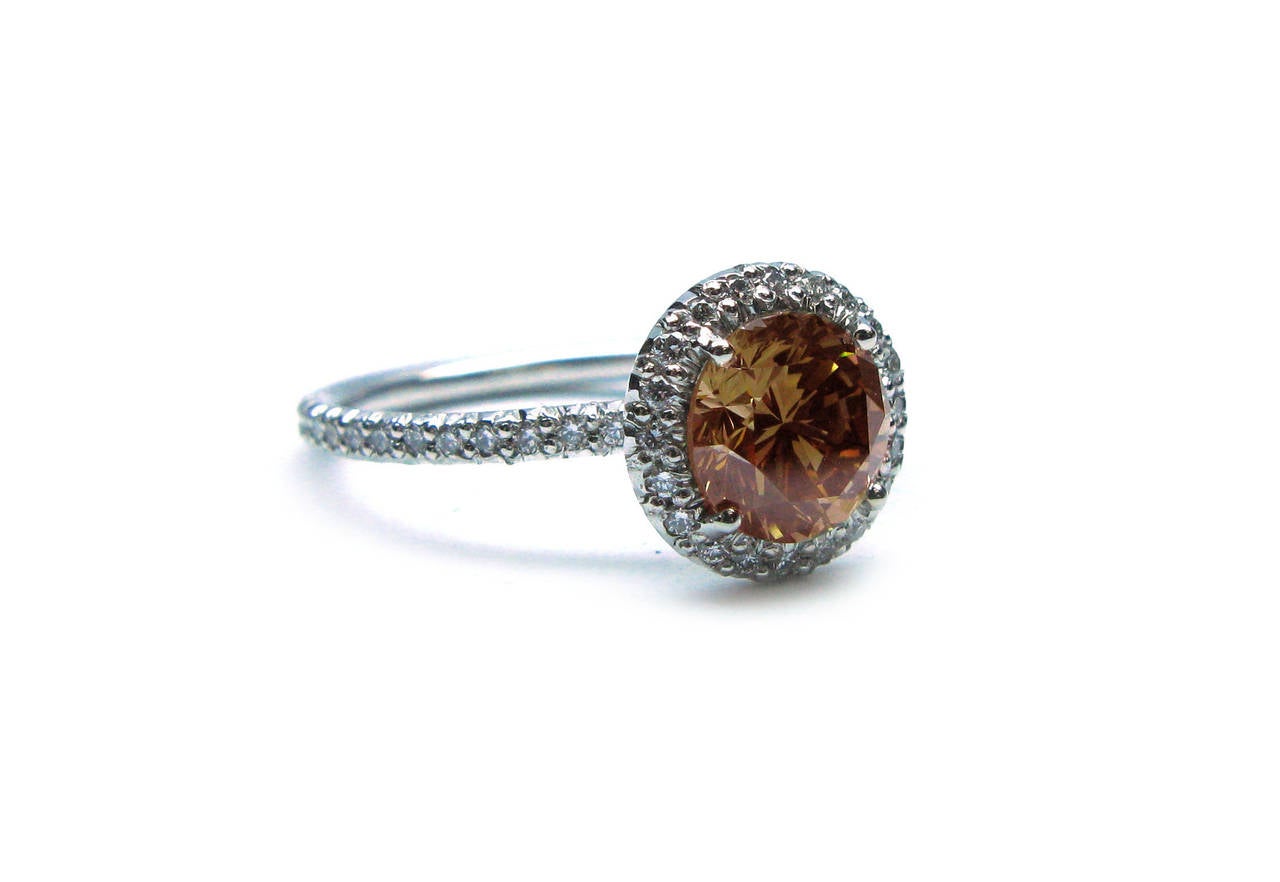 This fashion forward handmade platinum engagement ring features a 1.28ct, natural Fancy Brownish Orange color, VS1 clarity, Round Brilliant diamond center stone with a pave frame and band weighing 0.35cts. This is the perfect ring for a woman who