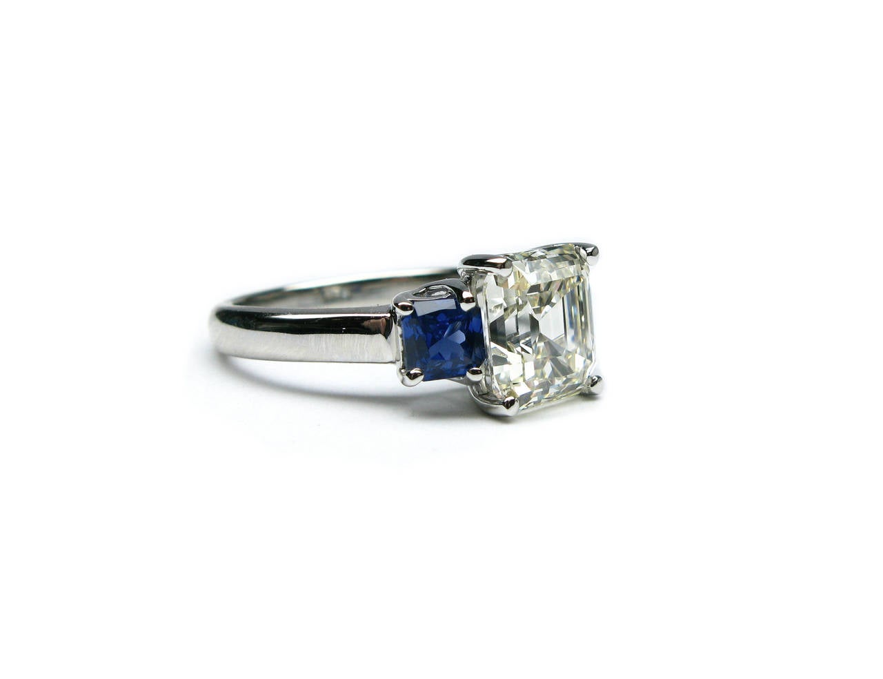 This  EGLUSA certified, 2.75Ct, J/K color, VS2 clarity Asscher cut diamond ring is set in platinum and flanked by two lovely vivid blue sapphires weighing approximately 1.00Ctw. The unexpected pop of color the sapphires contribute to this ring make