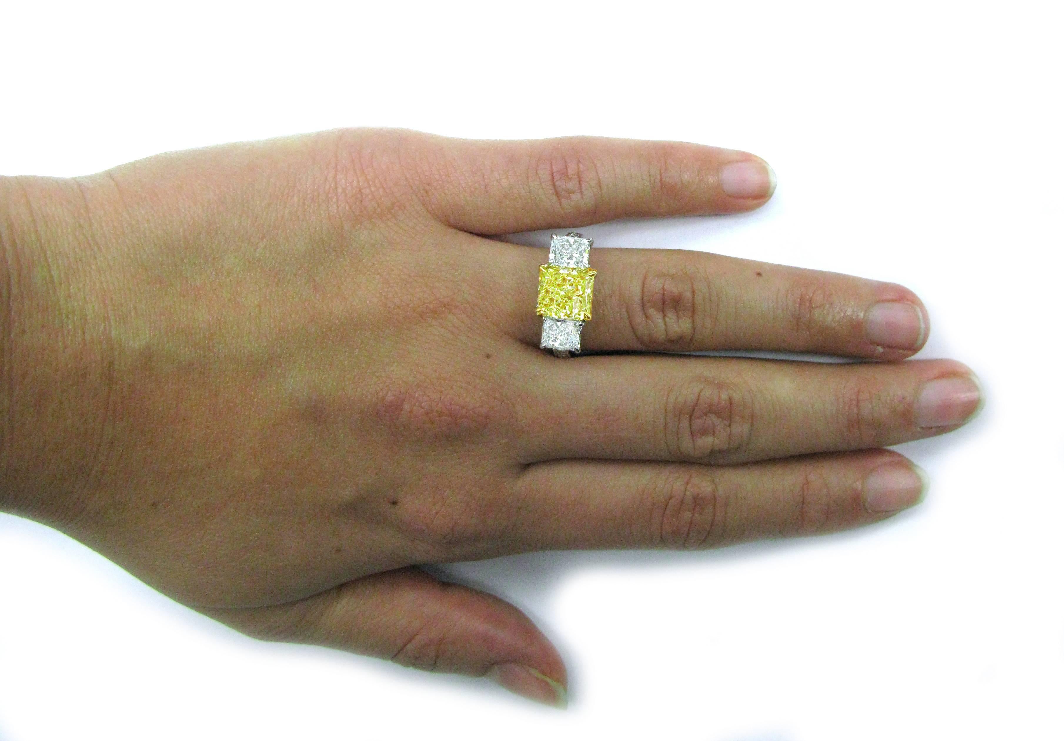 This lovely handmade 18kt yellow gold and platinum 3-stone diamond ring features a 2.51 carat, Fancy Yellow color, VVS2 clarity, radiant-cut diamond center stone with 1.48ctw, E/F color, VS clarity, Radiant cut diamond sidestones and 0.30ctw pave