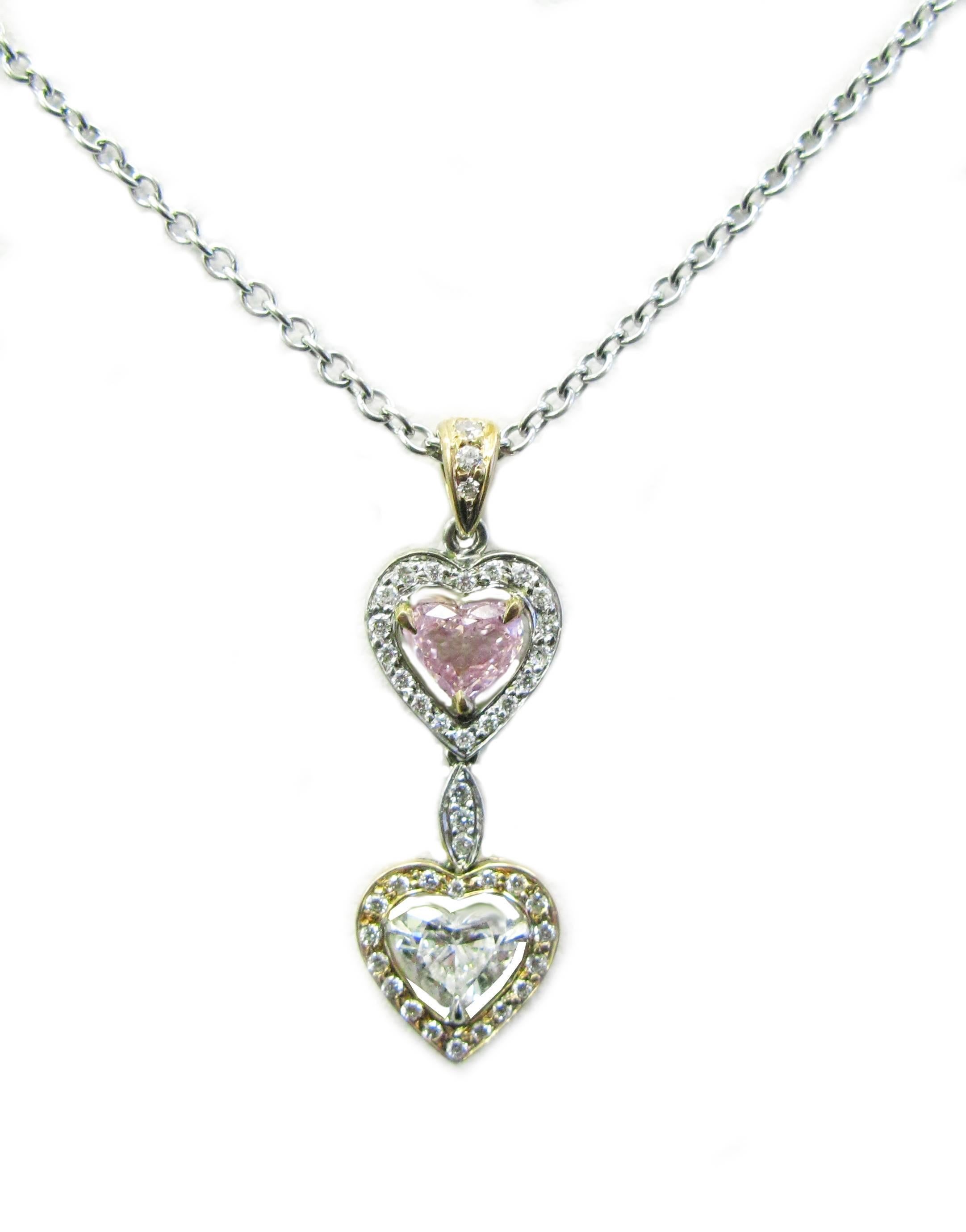 This beautiful 18kt two-tone gold pendant is unlike any other. It features a  GIA certified, 0.30ct, Natural Fancy Pink color, Heart shape diamond on top with a pave frame in white gold. The bottom Heart shape diamond is a 0.50ct, E/F color, VS