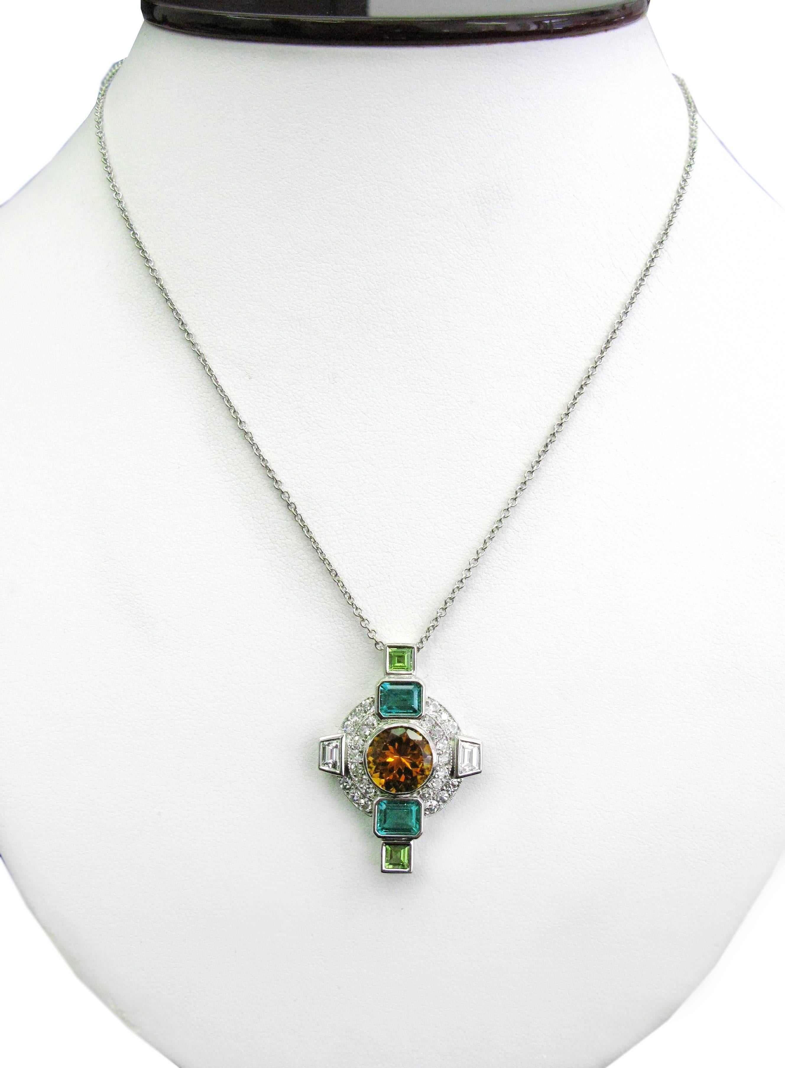 This stunning one-of-a-kind 18kt white gold cross pendant features a bezel set 3.53ct round brilliant citrine center stone with two bezel set step cut emeralds totaling 2cts and two asscher cut peridots totaling 1ct. The piece is completed with 13